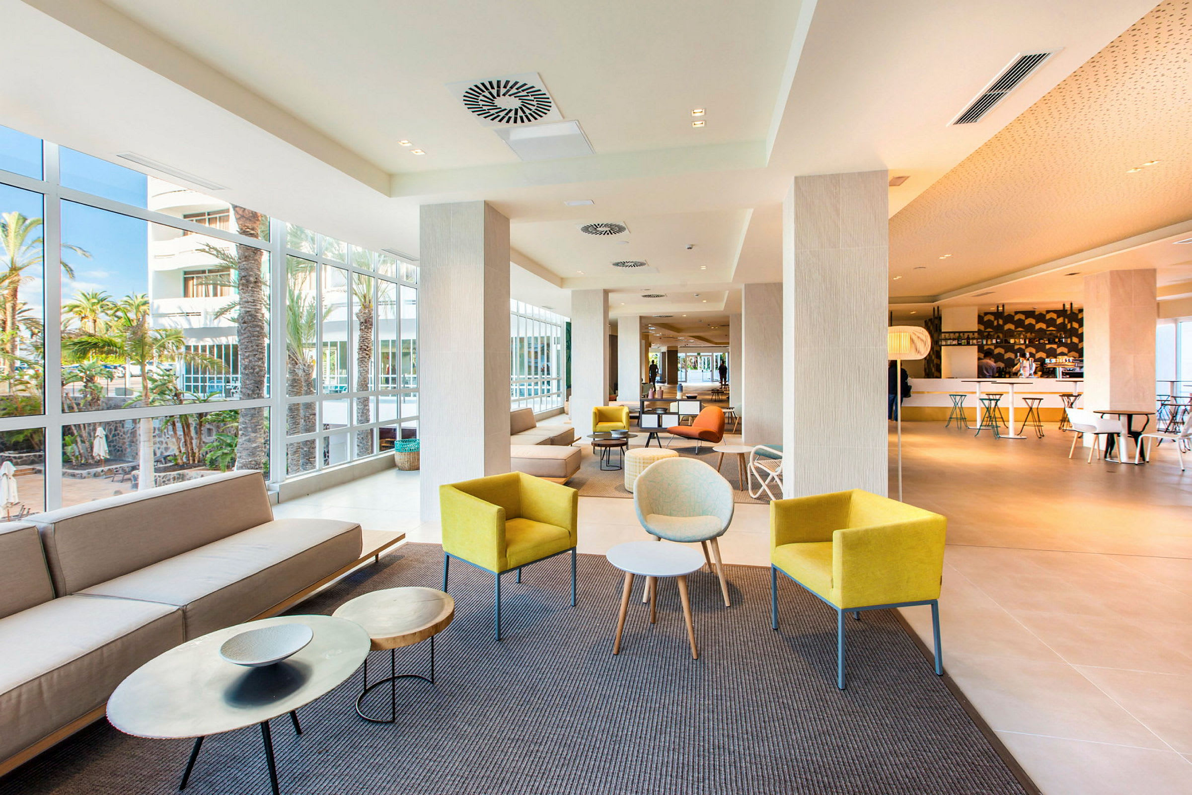 En lys hotellets lobby med forskellige siddeområder og store vinduer. (AI-genereret tekst)