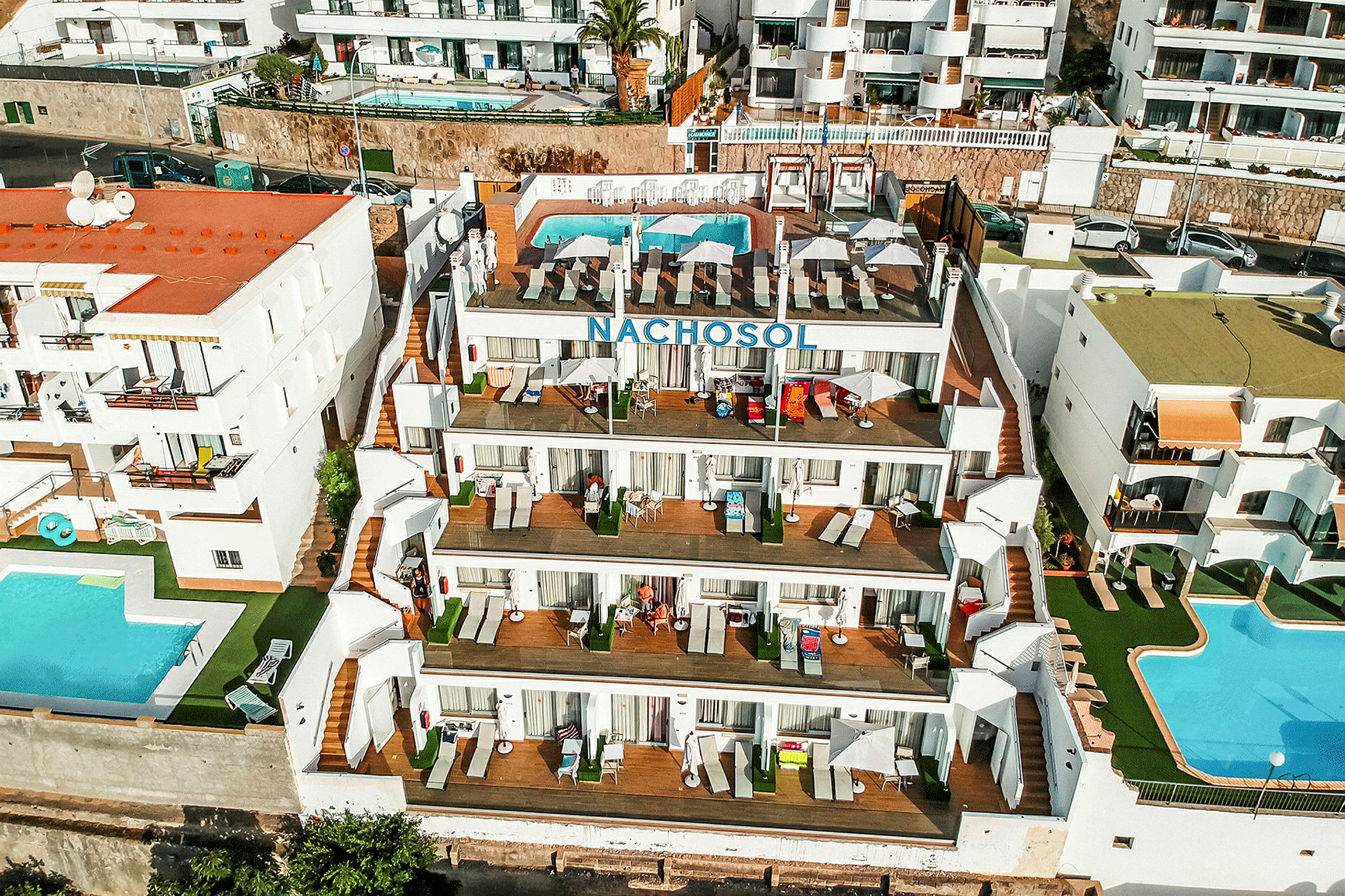 Hotel Nachosol med pool og altaner, omgivet af andre bygninger. (AI-genereret tekst)