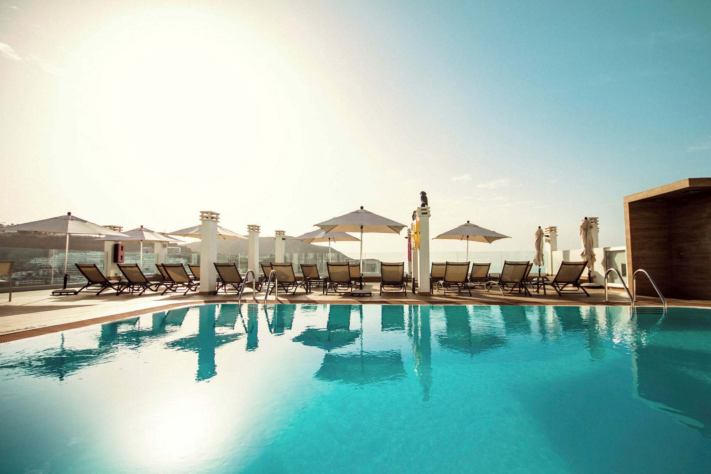 Udendørs pool på hotel med liggestole og parasoller. (AI-genereret tekst)