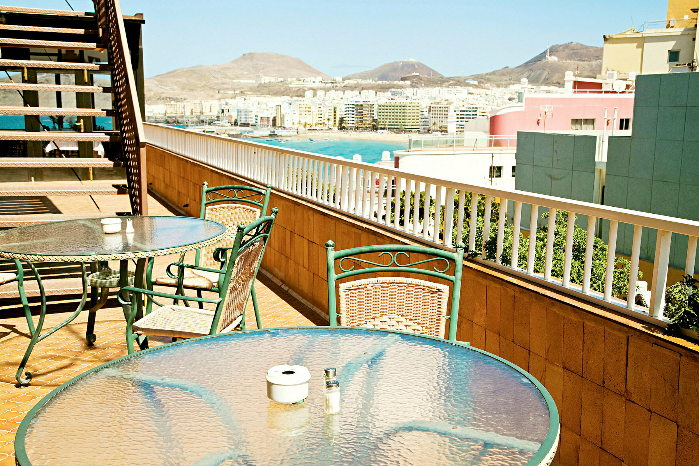 Bord og stole på en terrasse med udsigt over en by og bjerge. (AI-genereret tekst)