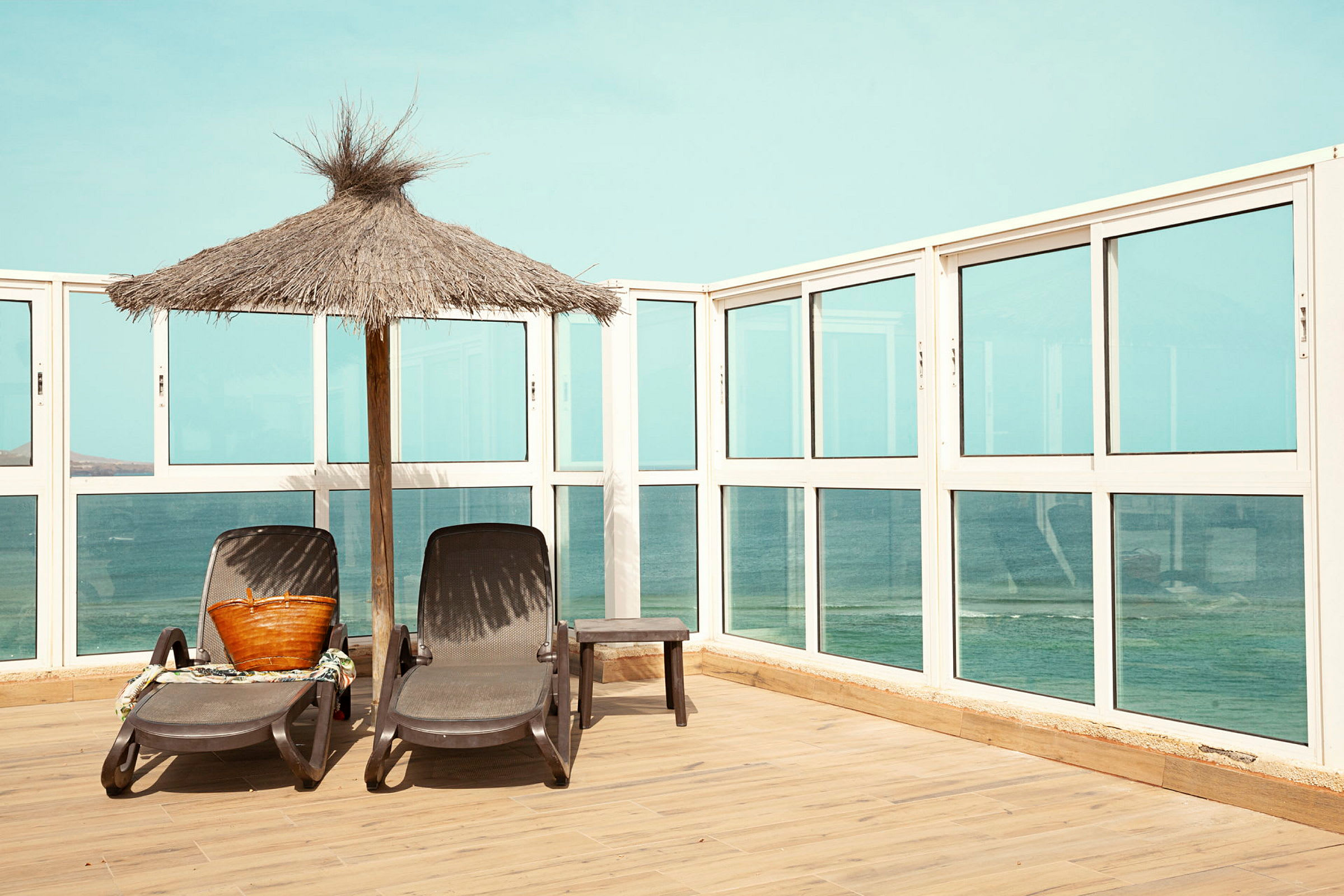 To liggestole står ved siden af en parasol på en terrasse med udsigt over havet. (AI-genereret tekst)