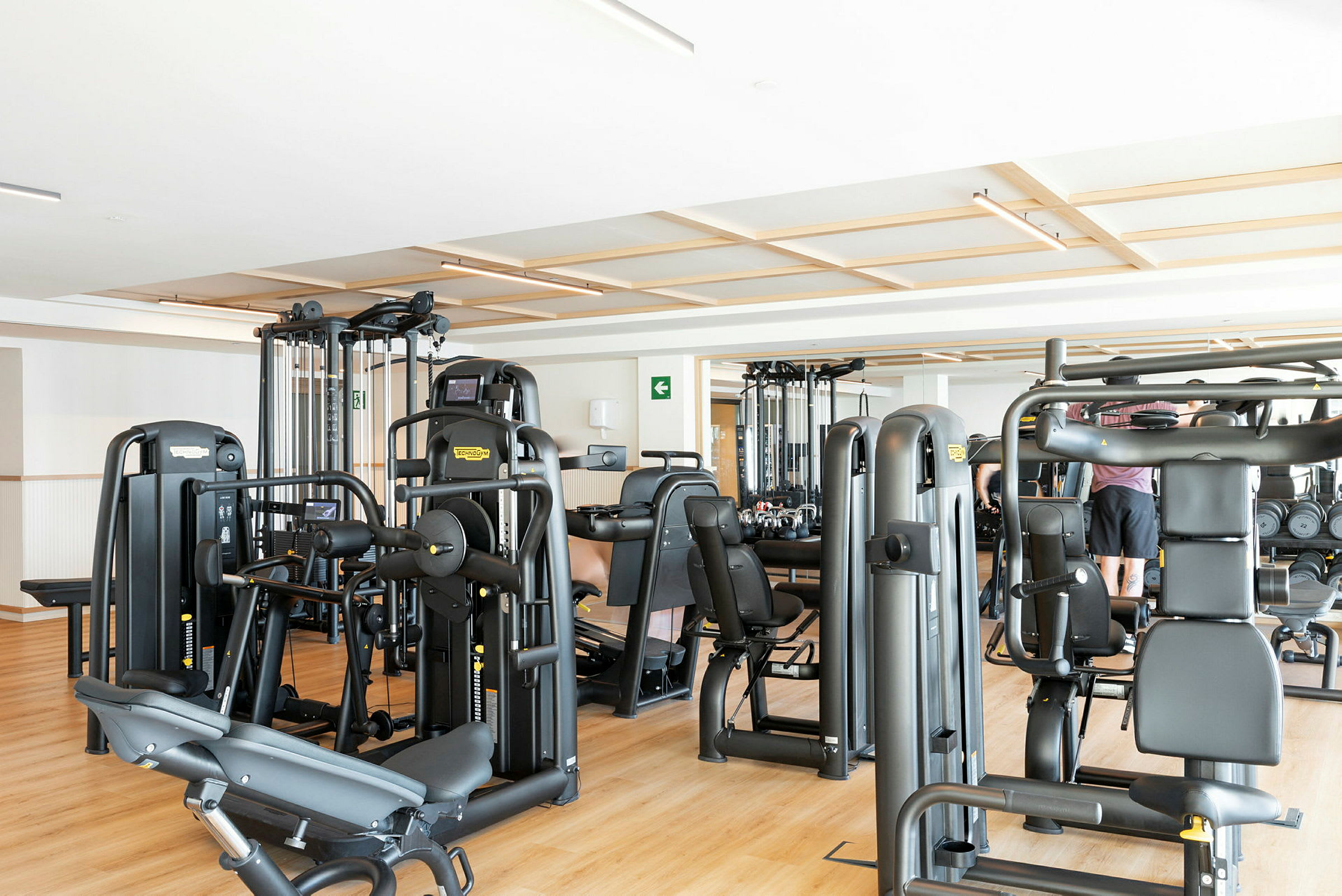 Billede af et fitnesscenter med træningsmaskiner og nogle personer. (AI-genereret tekst)
