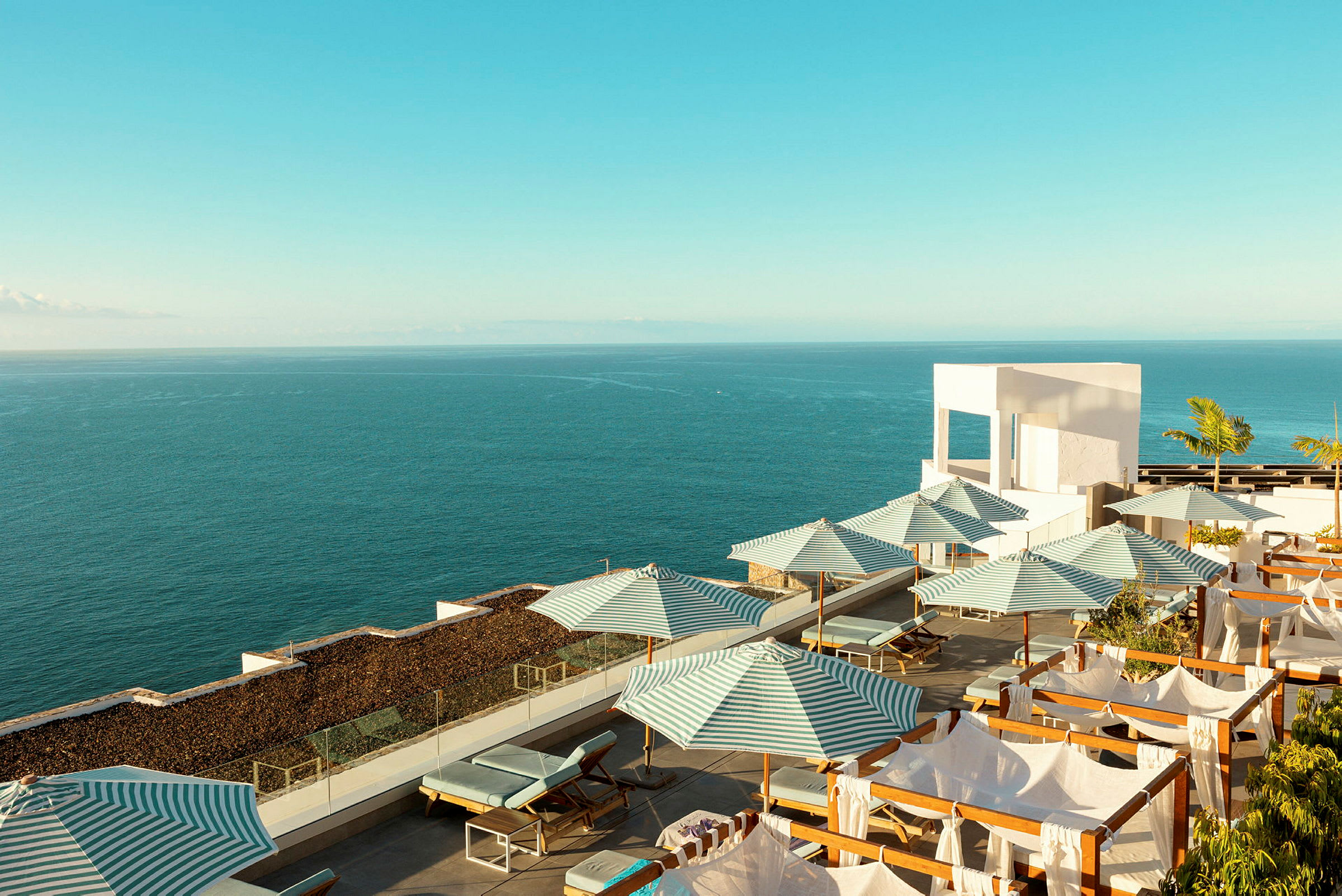 Solstole og stribede parasoller på en terrasse ved havet. (AI-genereret tekst)