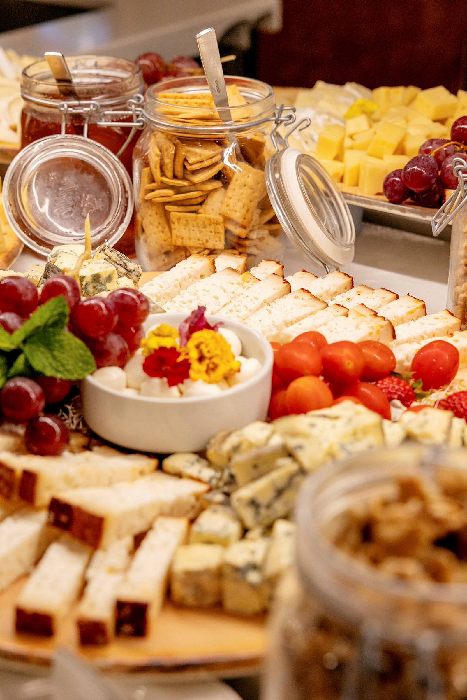 Et udvalg af forskellige oste, kiks, druer og små tomater på en buffet. (AI-genereret tekst)