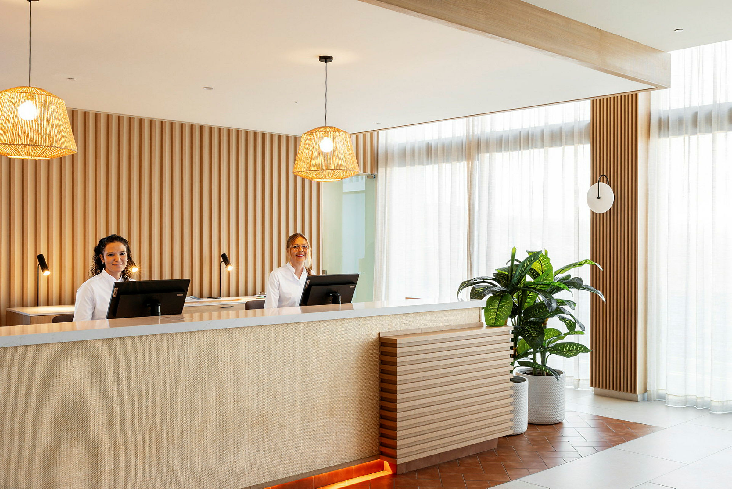 Reception med to arbejdsstationer, hængende lamper og dekorativ plante. (AI-genereret tekst)