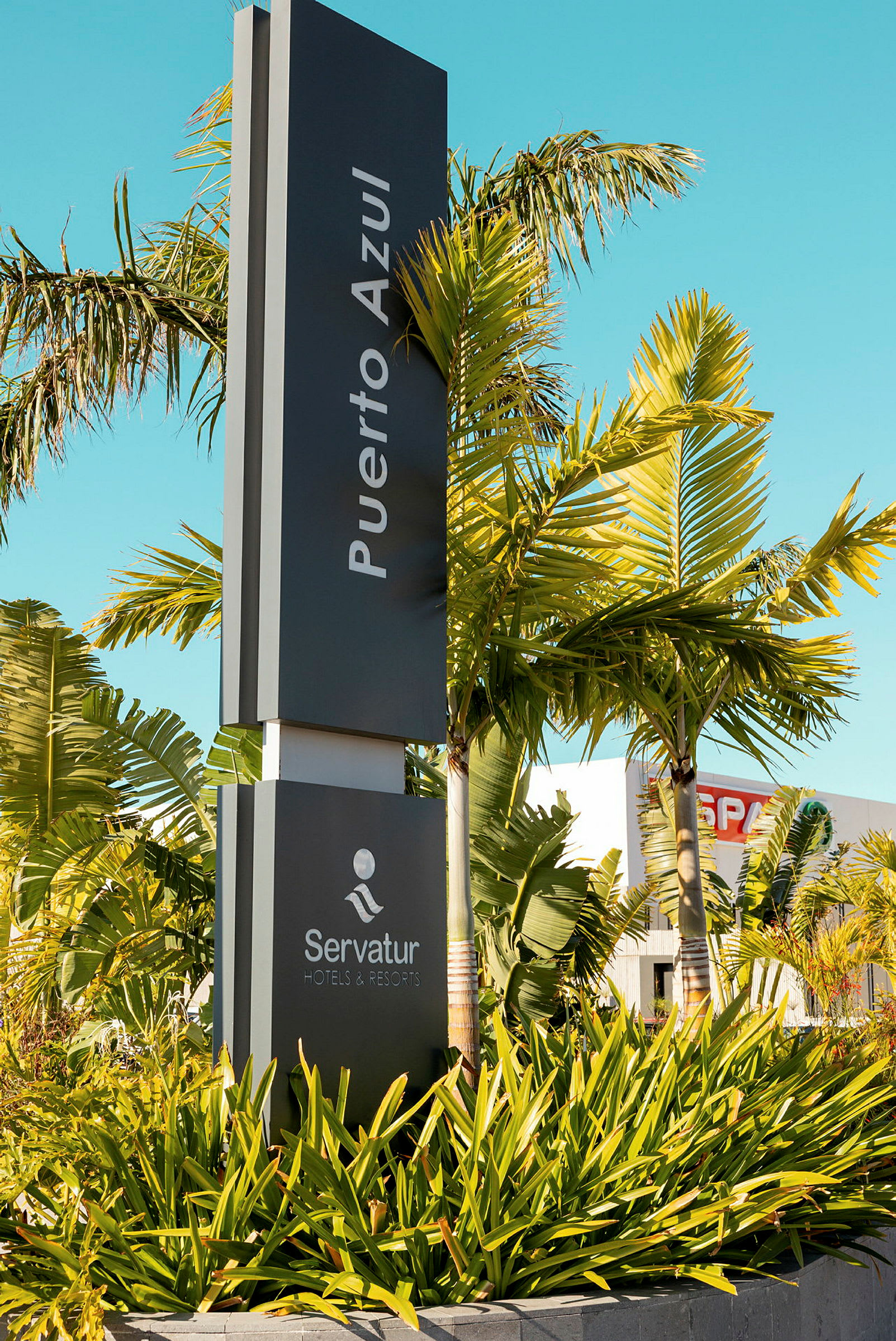 Skilt med teksten 'Puerto Azul' og 'Servatur Hotels & Resorts', omgivet af palmer og vegetation. (AI-genereret tekst)