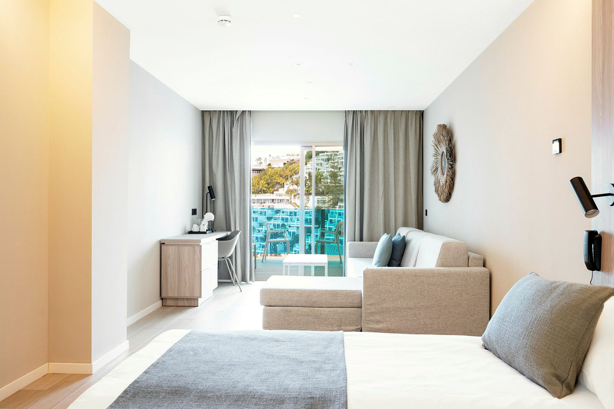 Moderne hotelværelse med seng, sofa og skrivebord samt en altan med udsigt. (AI-genereret tekst)