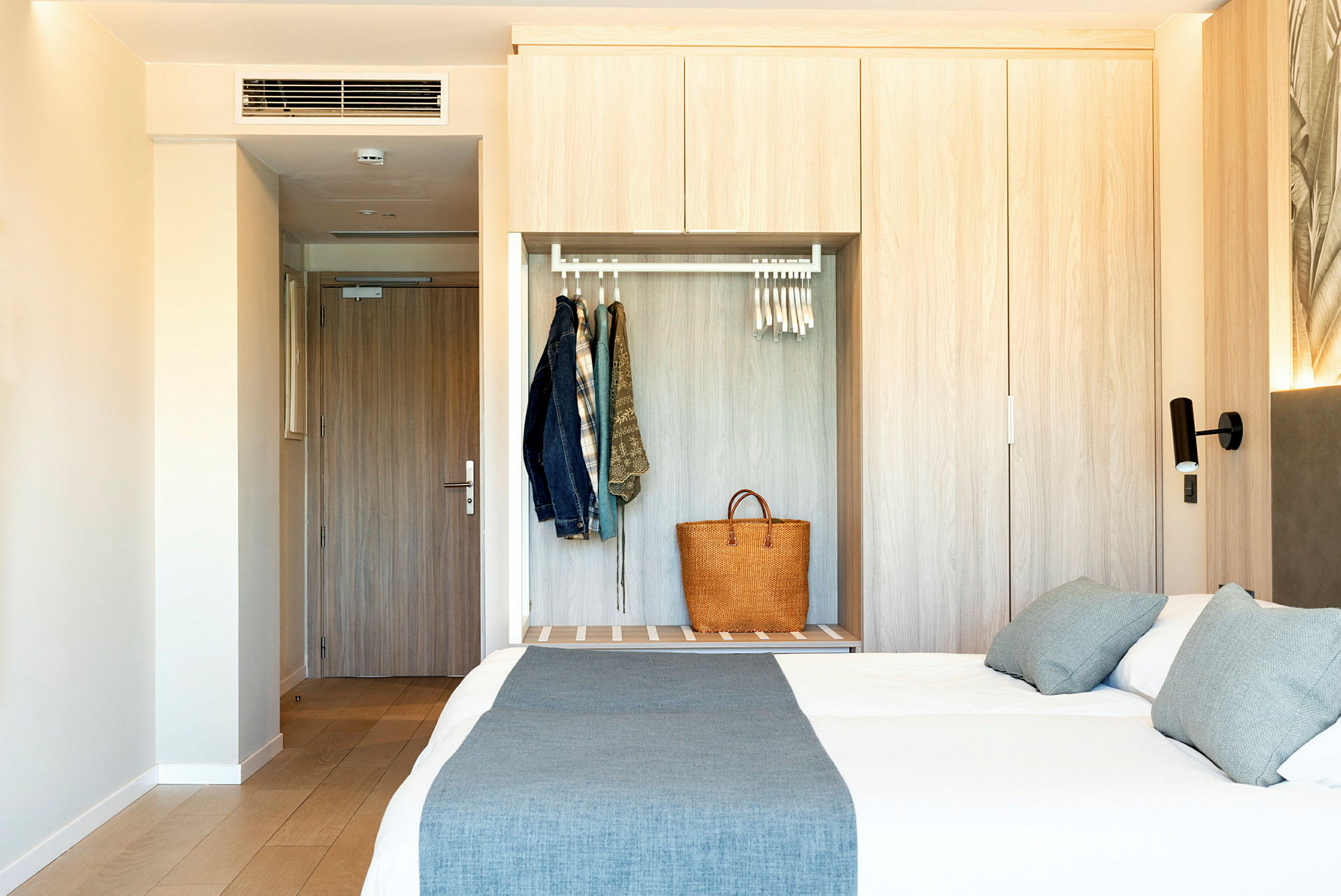 Et hotelværelse med en dør, garderobe og en redt dobbeltseng. (AI-genereret tekst)