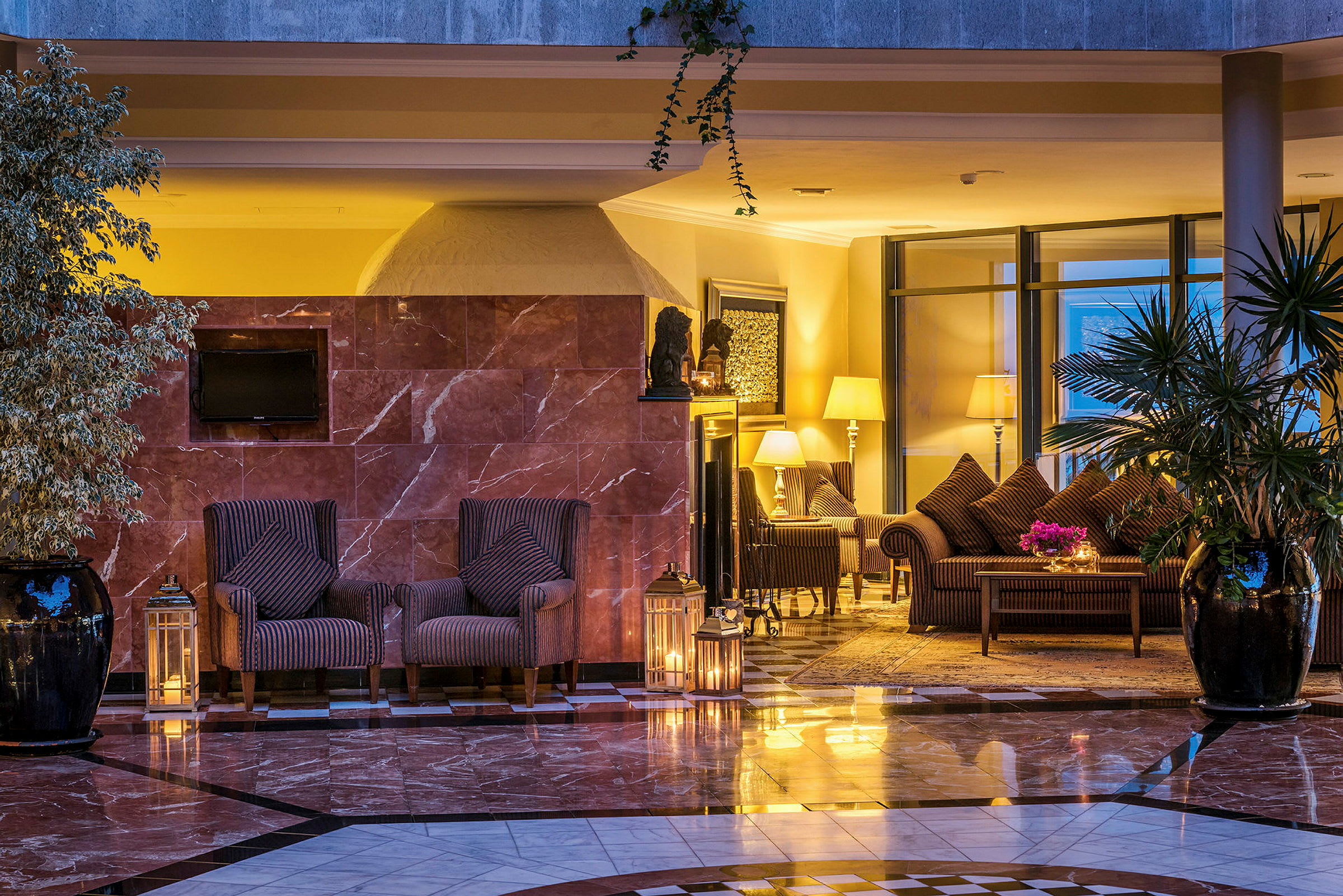 Et hotelværelse med elegant indretning, herunder lænestole, borde, lampeskærme og planter. (AI-genereret tekst)
