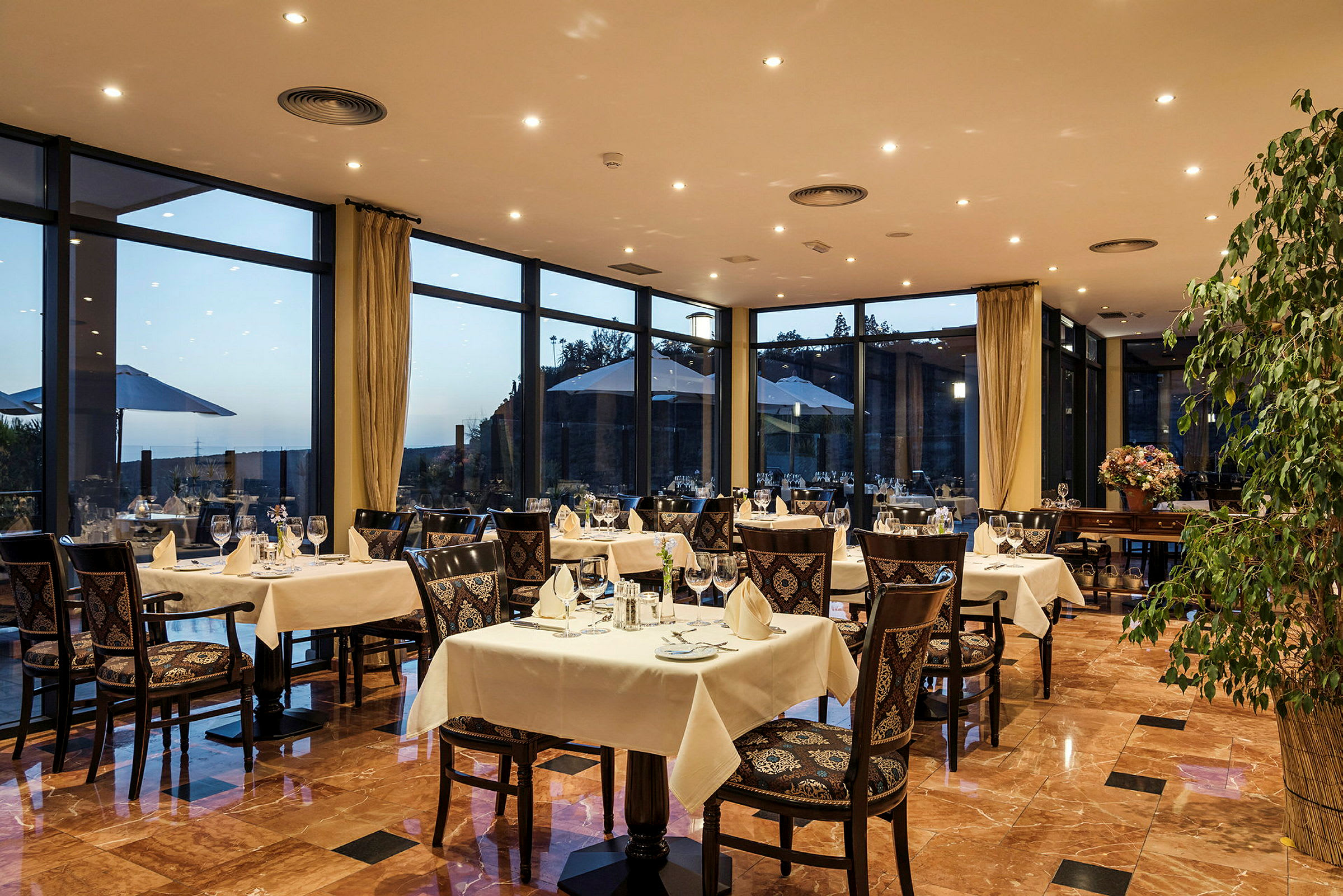 Restaurant med dækkede borde og udsigt gennem store vinduer. (AI-genereret tekst)