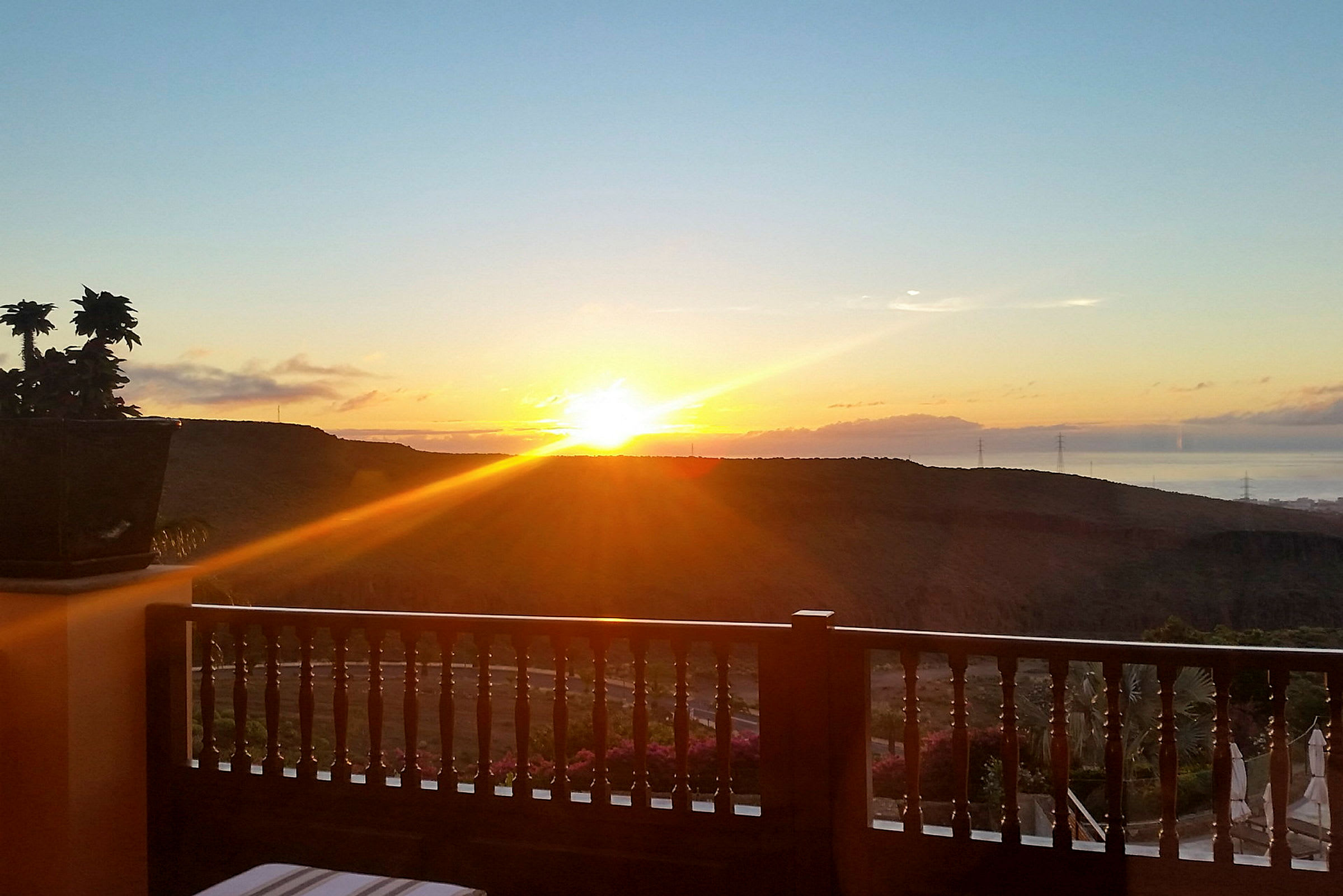 Solnedgang over et landskab med bakker, set fra en altan med trægelænder. (AI-genereret tekst)