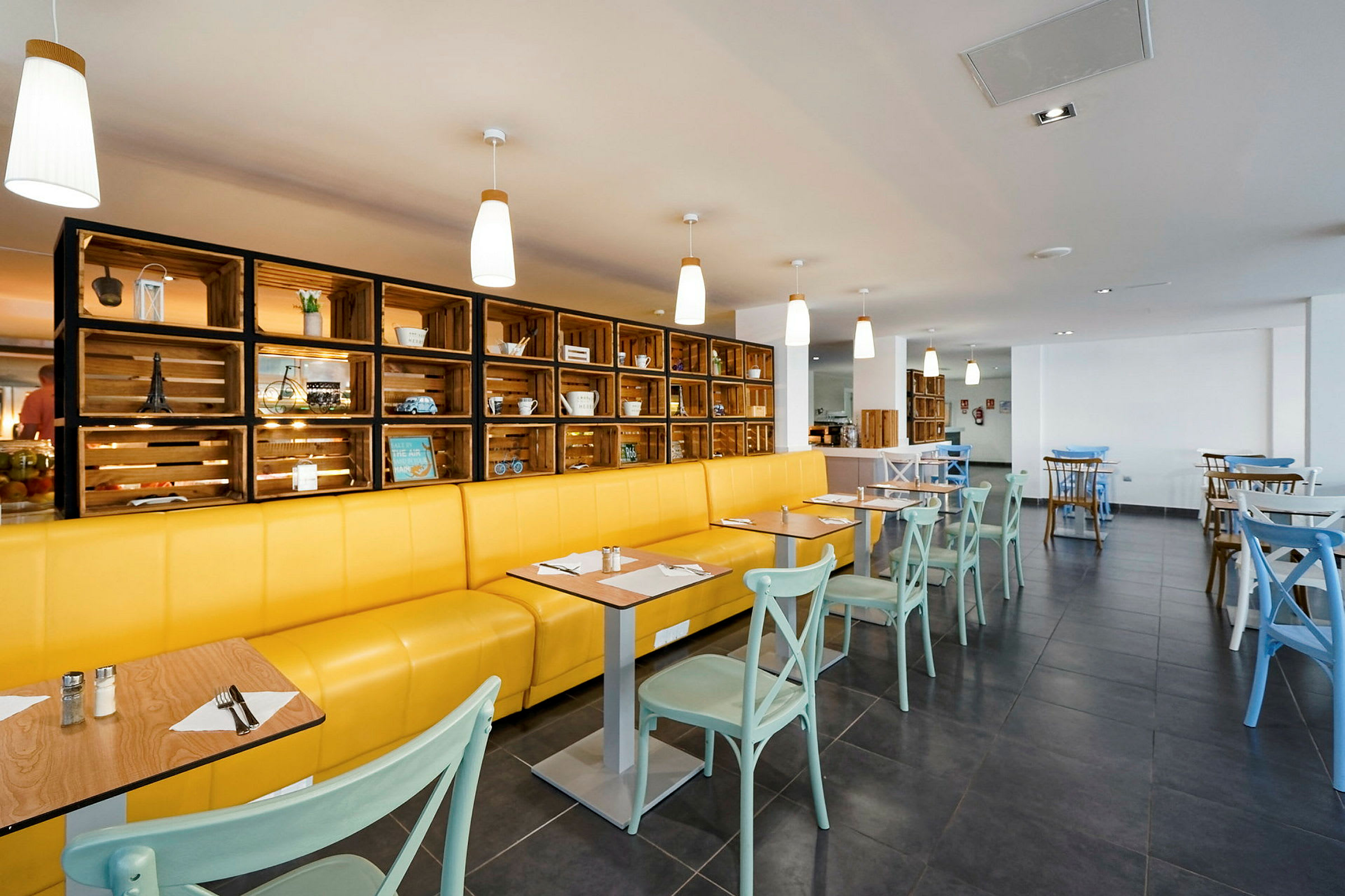 Restaurant med gul sofa, lyse stole og dekorativ træhylde. (AI-genereret tekst)