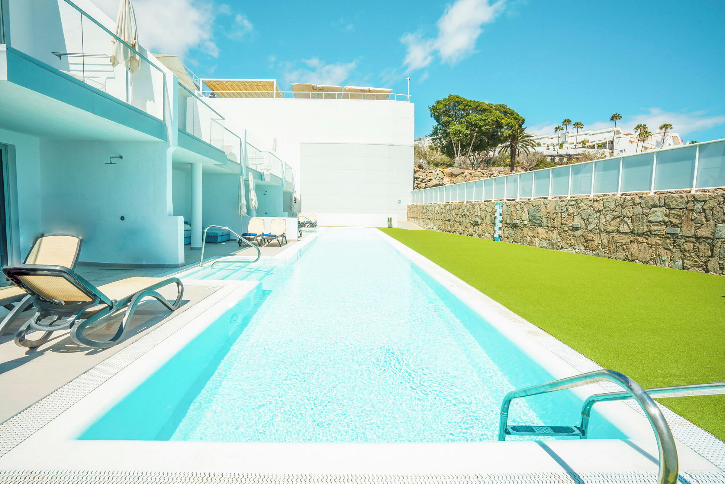 En lang swimmingpool med liggestole ved siden og en grøn græsplæne. (AI-genereret tekst)