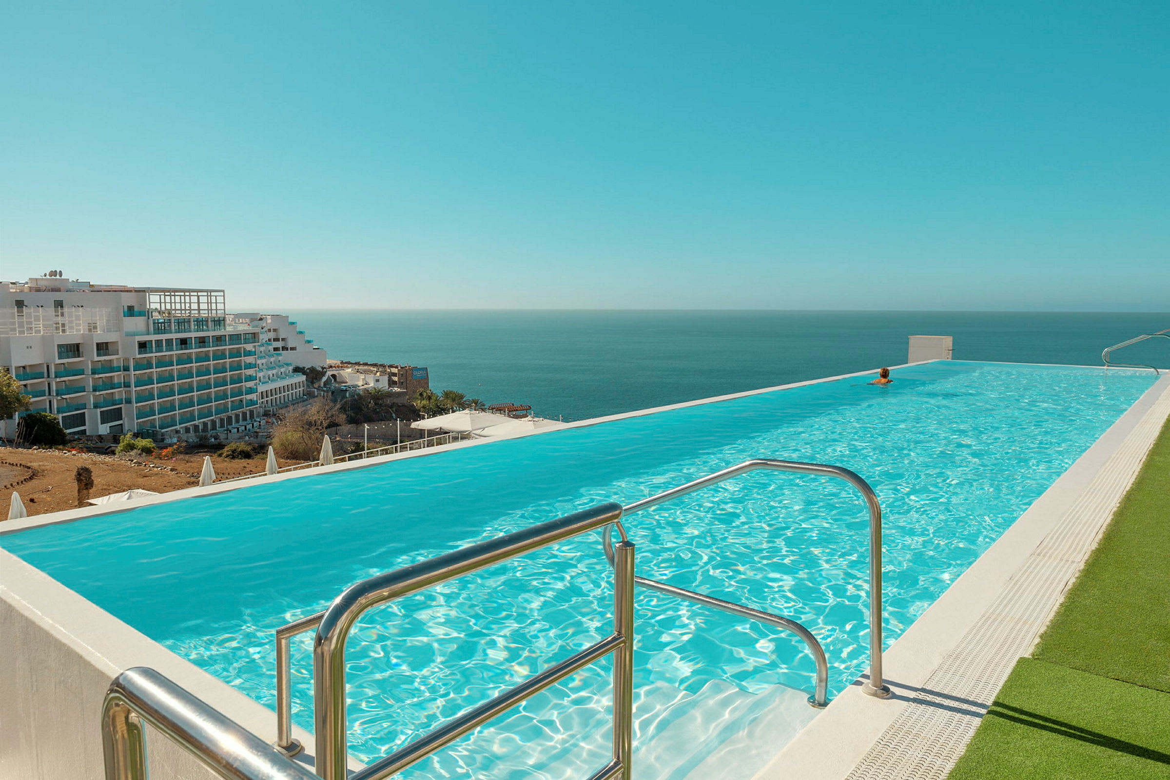 Infinitypool med udsigt til havet. Bygninger synlige i baggrunden. (AI-genereret tekst)