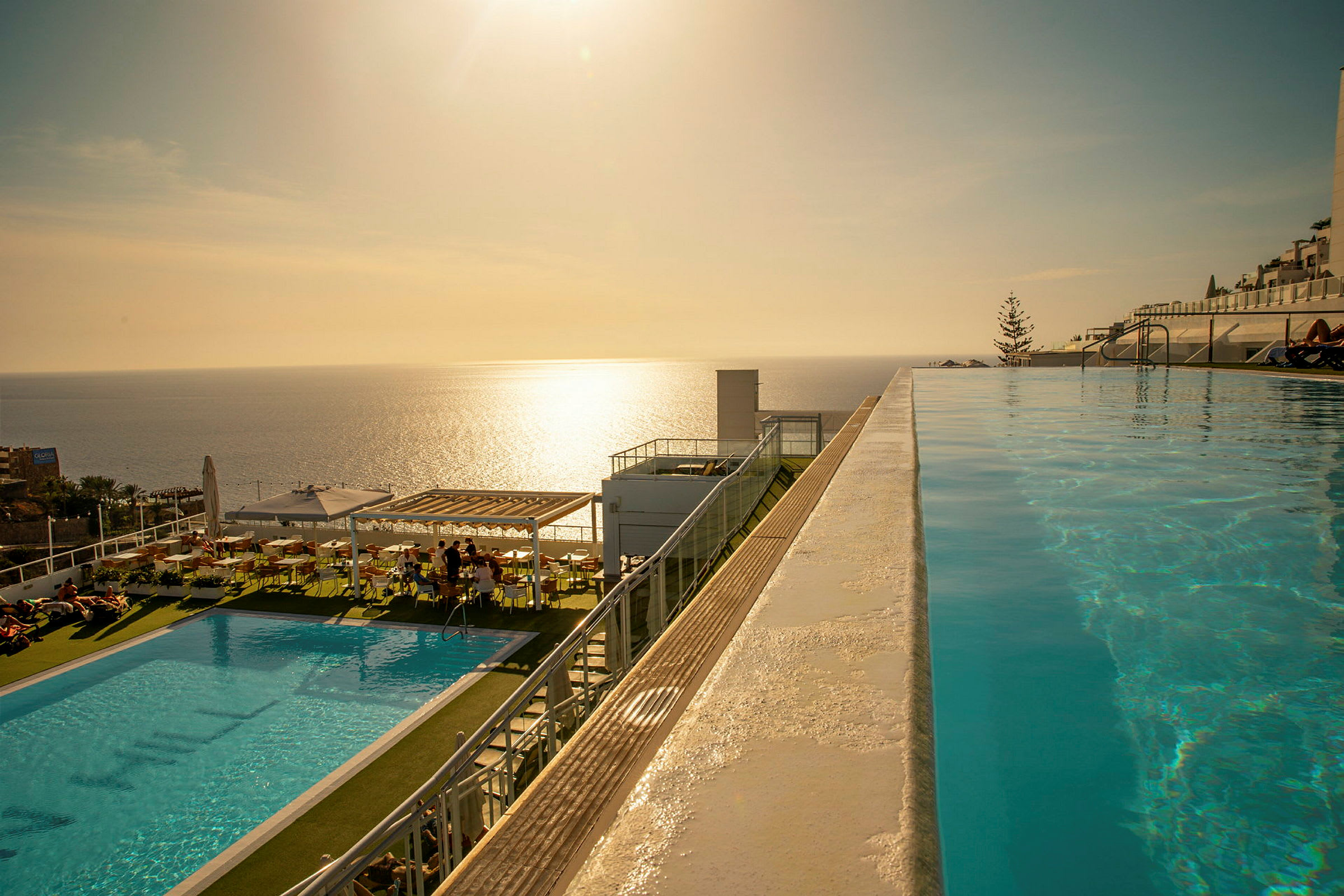 Infinitypool med udsigt over havet ved solnedgang, med siddepladser og en mindre pool ved siden af. (AI-genereret tekst)