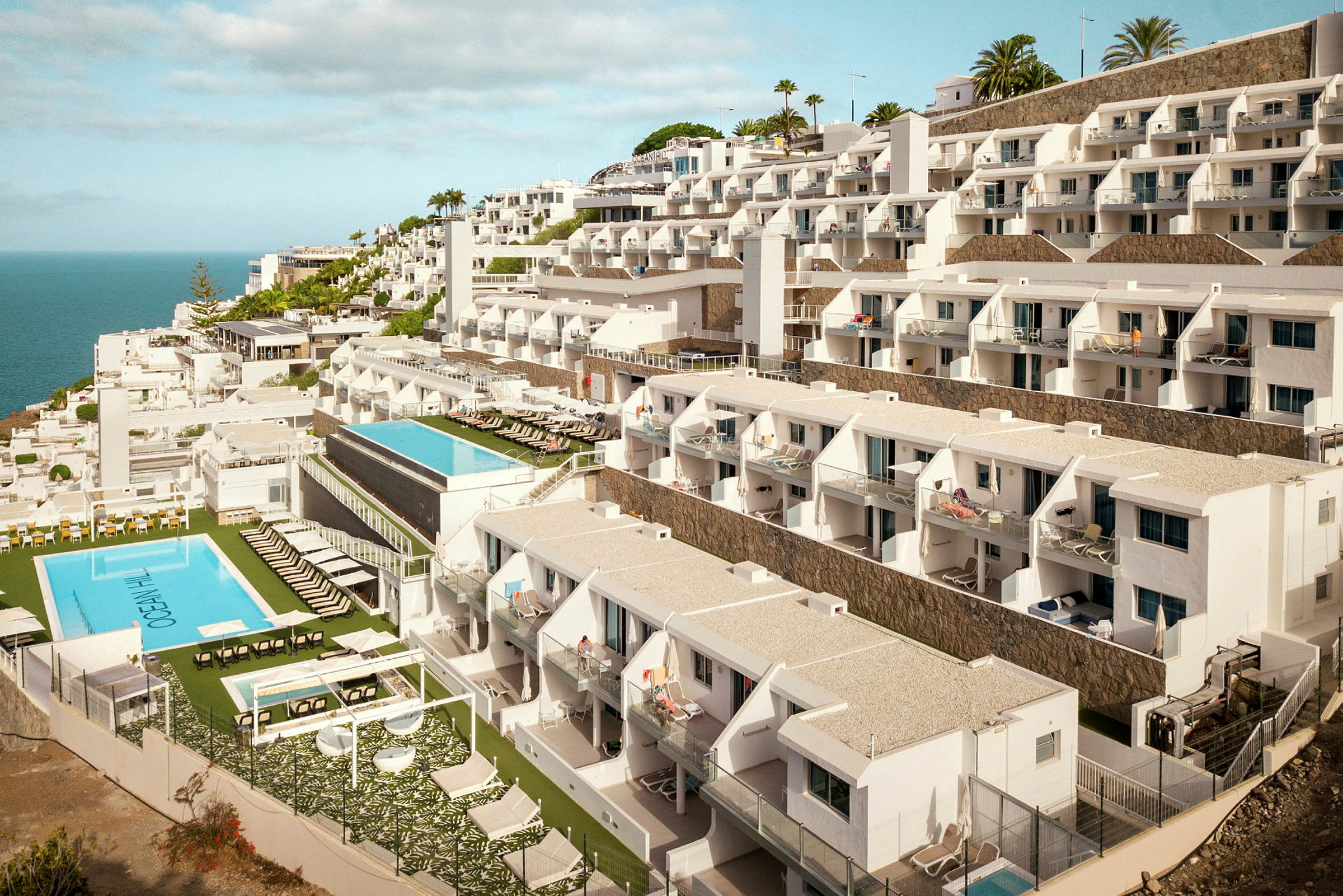 Hotelbygning med flere etager og pools mod havet. (AI-genereret tekst)