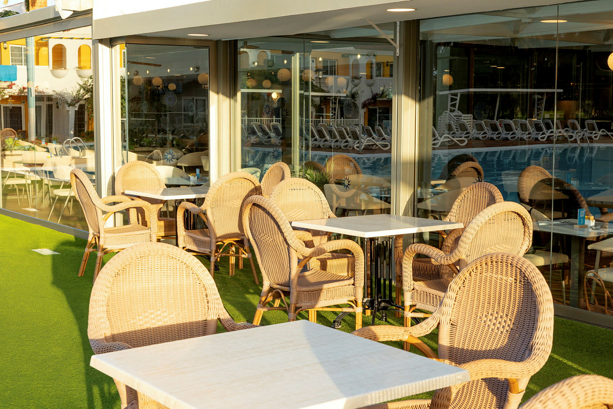 Udendørsmøbler ved en café eller restaurant, med flettede stole og borde, placeret ved store vinduer. (AI-genereret tekst)