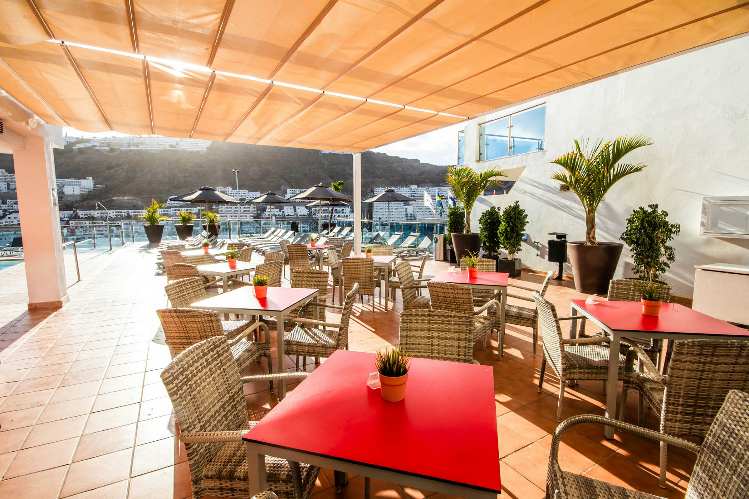 Terrasse med borde og stole, udsigt over pool og bygninger i baggrunden. (AI-genereret tekst)