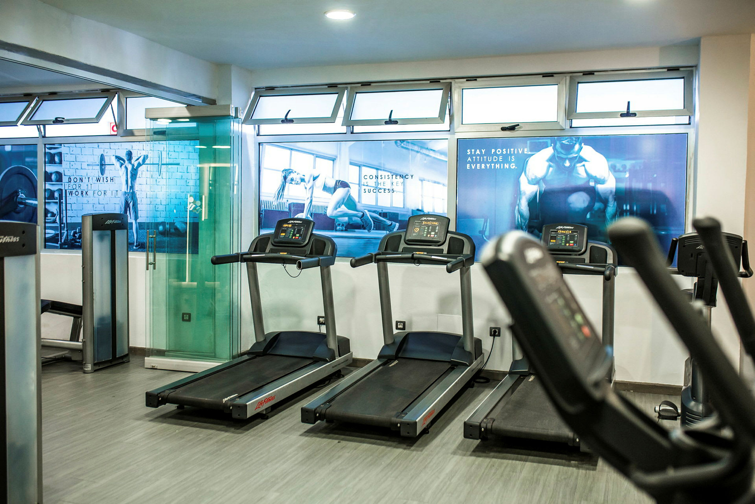 Et fitnesscenter med løbebånd og træningsmaskiner. Motiverende billeder er hængt op på væggene. (AI-genereret tekst)