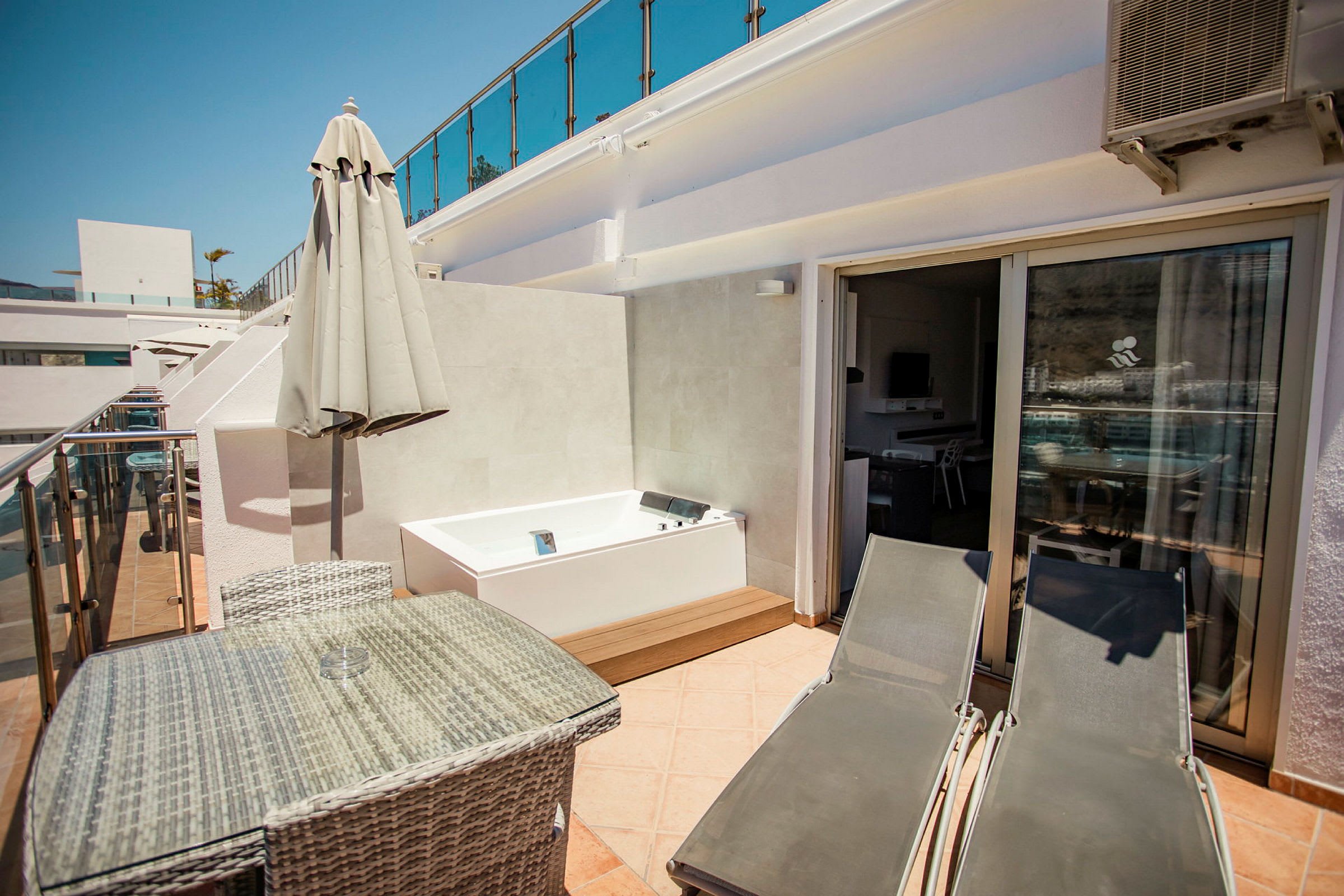 Privat terrasse med bord, stole, liggestole og en jacuzzi. (AI-genereret tekst)
