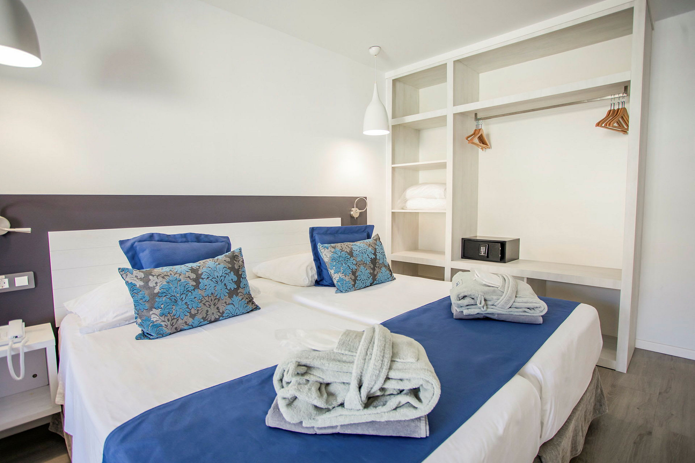 Billede af et hotelværelse med moderne design og en dobbeltseng med hvidt og blåt sengetøj. (AI-genereret tekst)