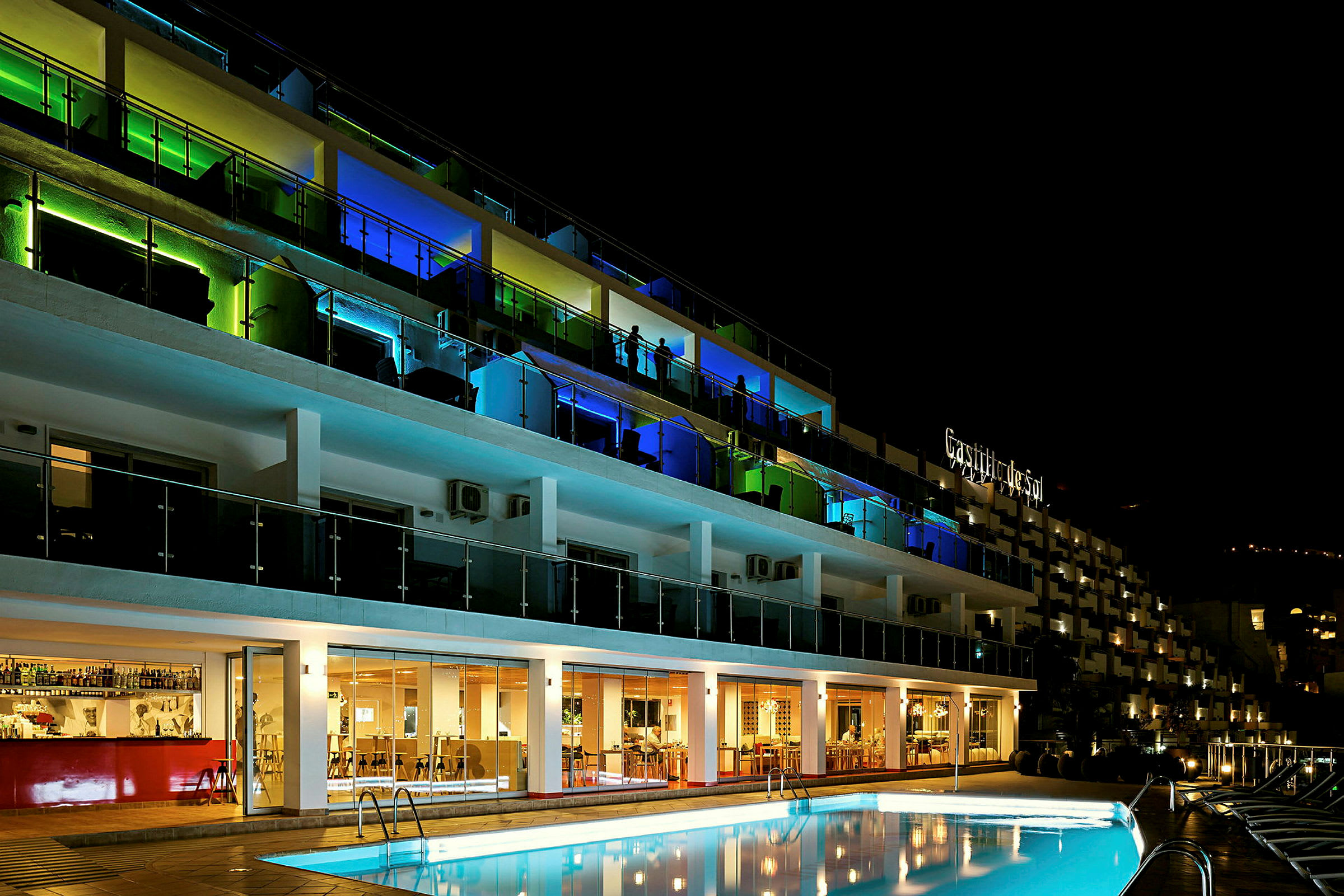 Et hotel med farverige lys på altanerne og en swimmingpool i forgrunden, fotograferet om natten. (AI-genereret tekst)