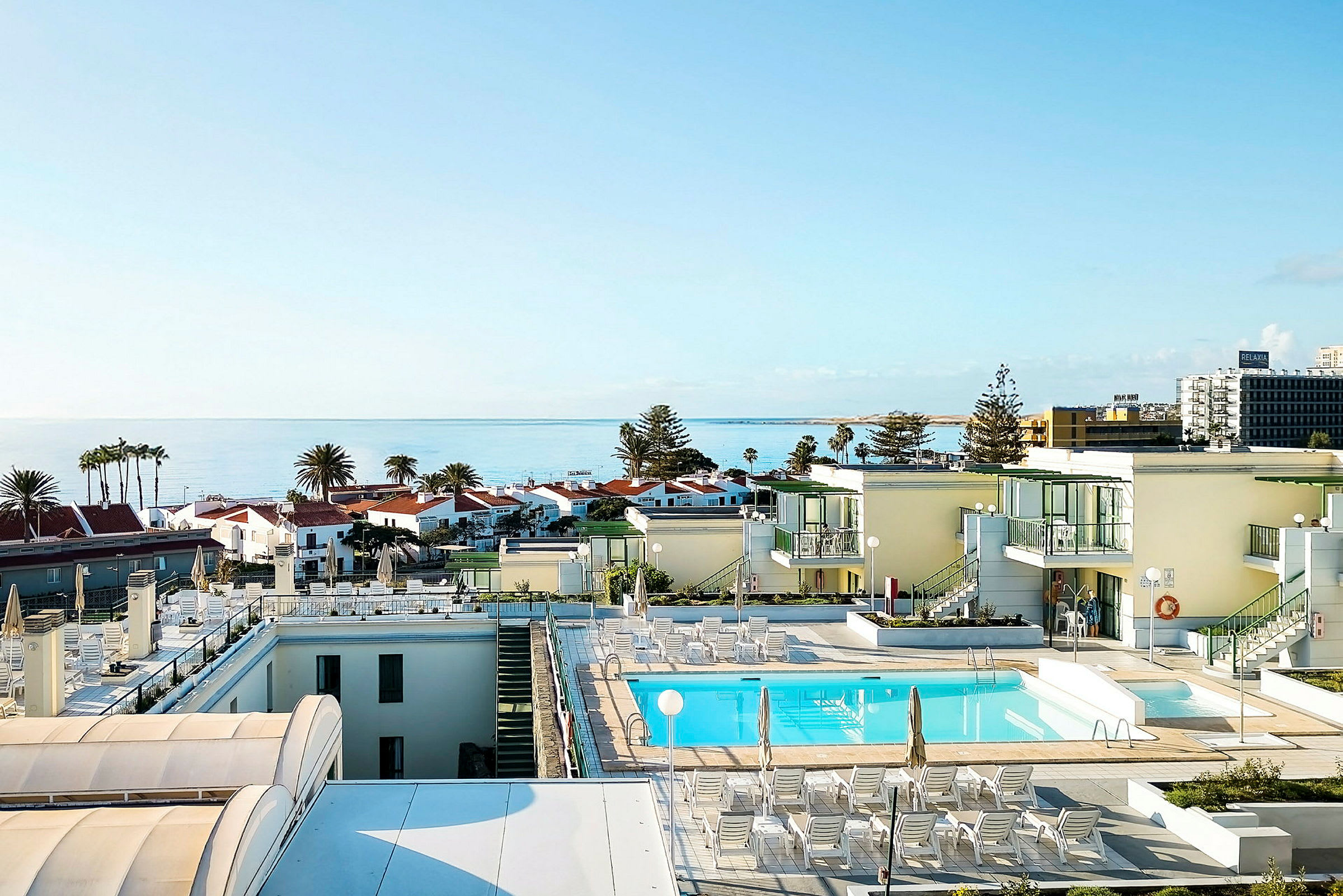 Udsigt over en pool på et hotel med havet og bygninger i baggrunden. (AI-genereret tekst)