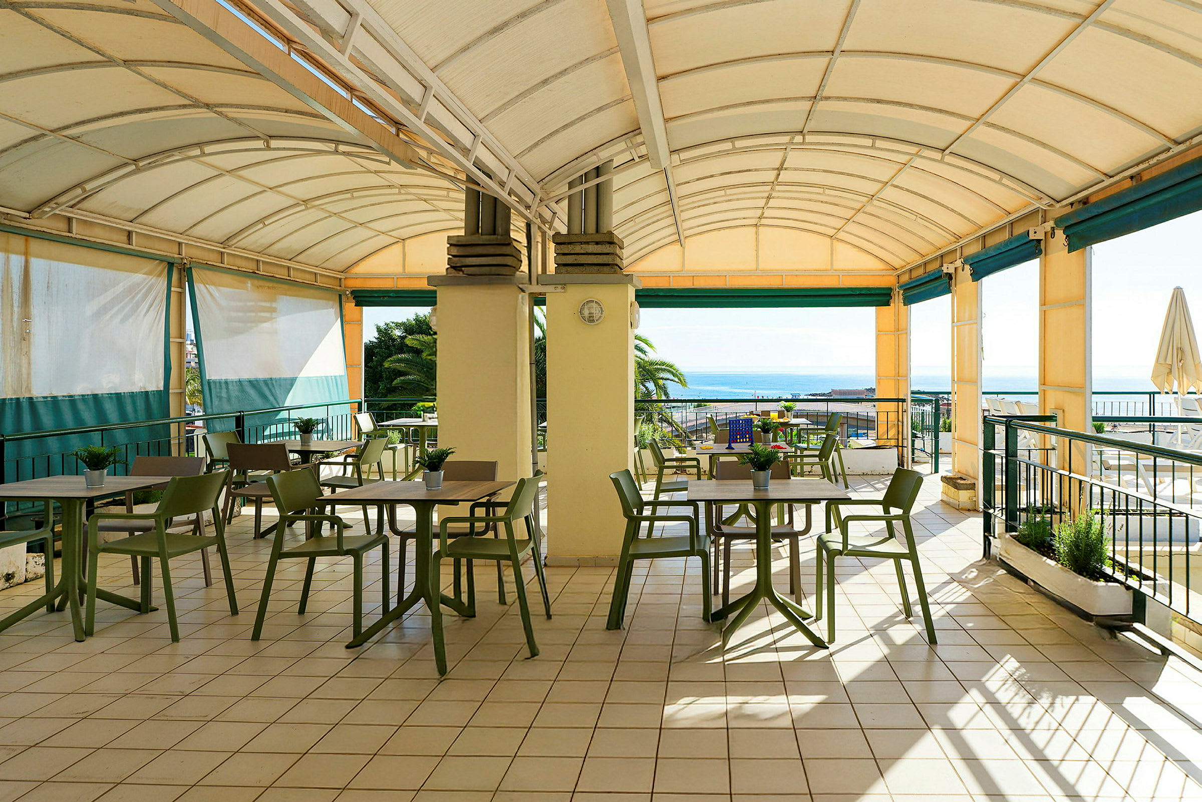 En overdækket terrasse med borde og stole, med udsigt over havet. (AI-genereret tekst)
