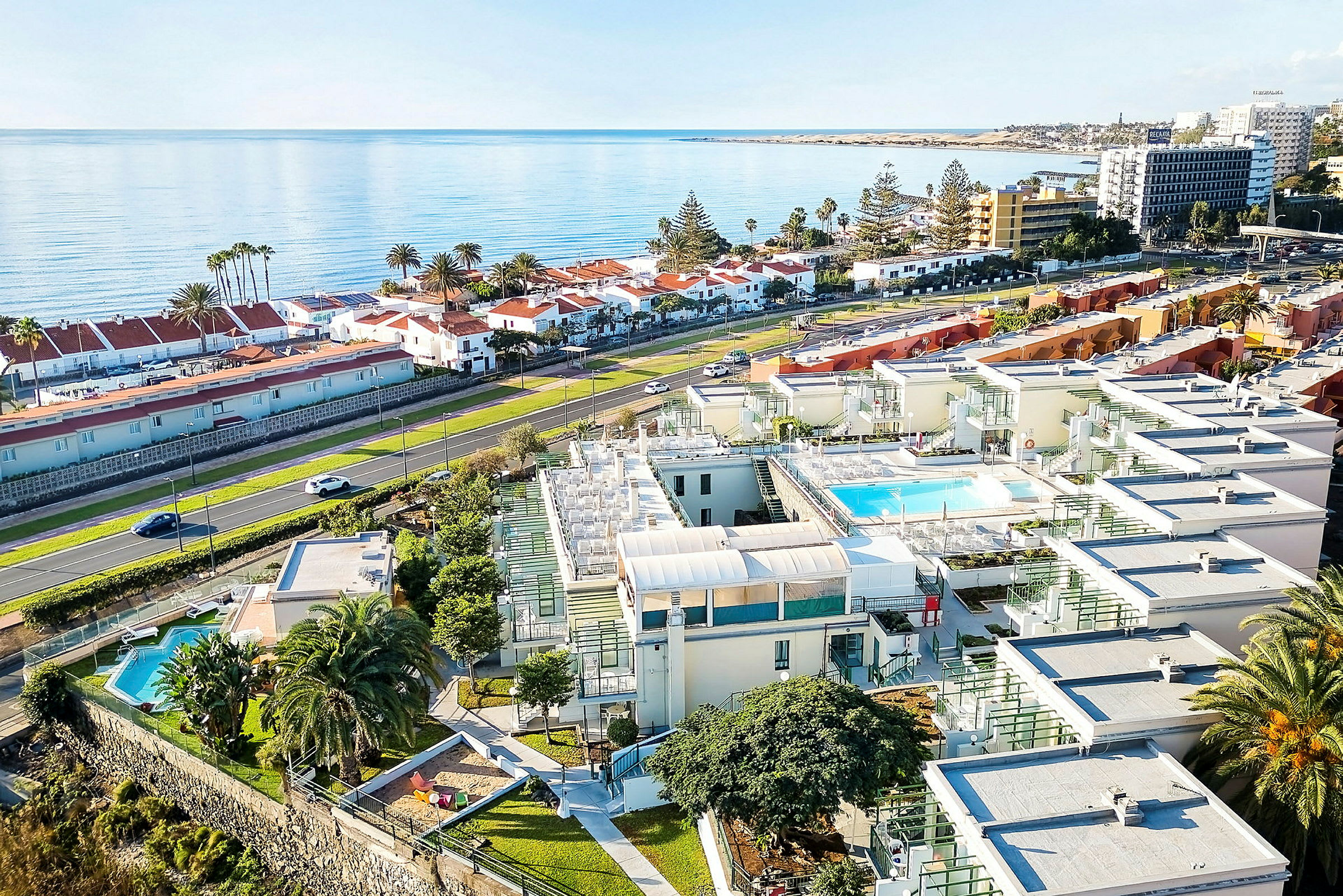 Luftfoto af resortområde med swimmingpools og bygninger tæt på havet. (AI-genereret tekst)