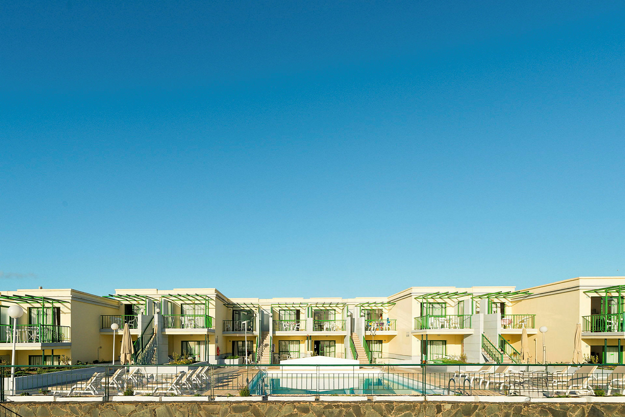 Et hotelkompleks med moderne bygninger med grønne detaljer og en pool foran. (AI-genereret tekst)