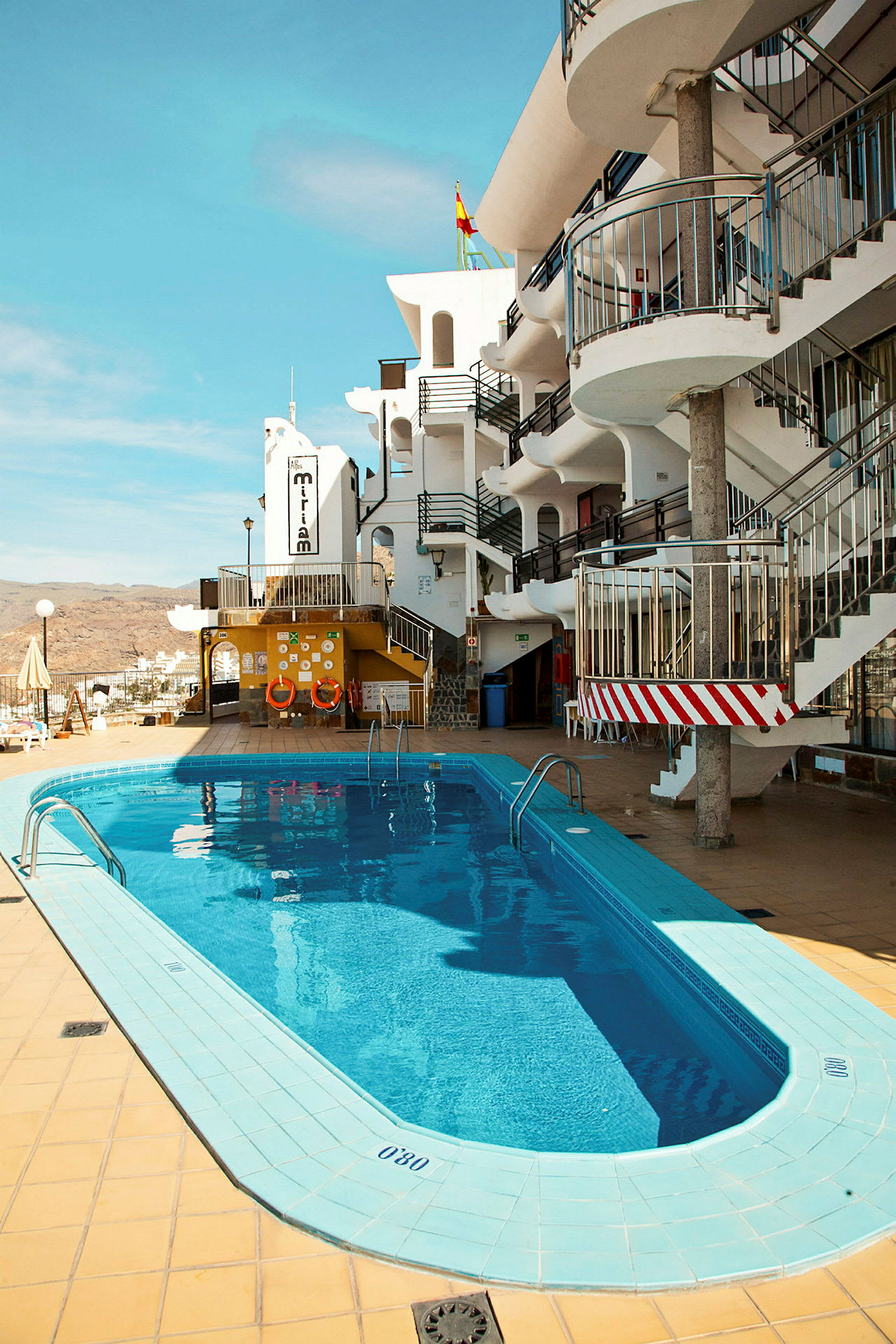 Udendørs pool ved hotel med hvid bygning og blå himmel. (AI-genereret tekst)