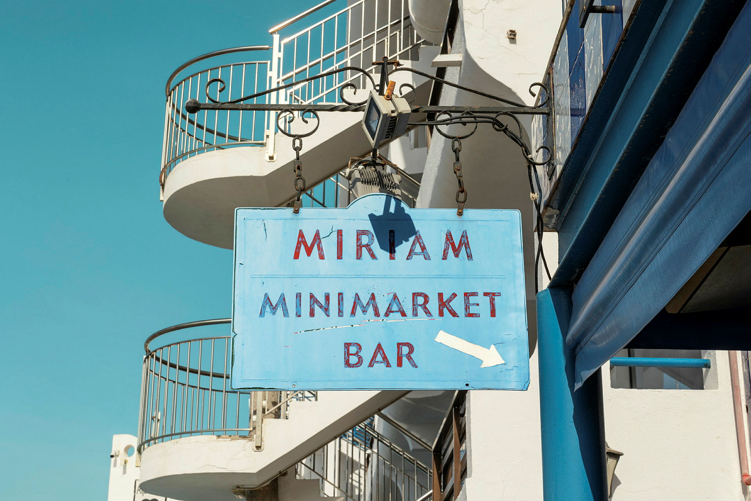 Skilt med teksten 'Miriam Minimarket Bar' hængende på en bygning. (AI-genereret tekst)