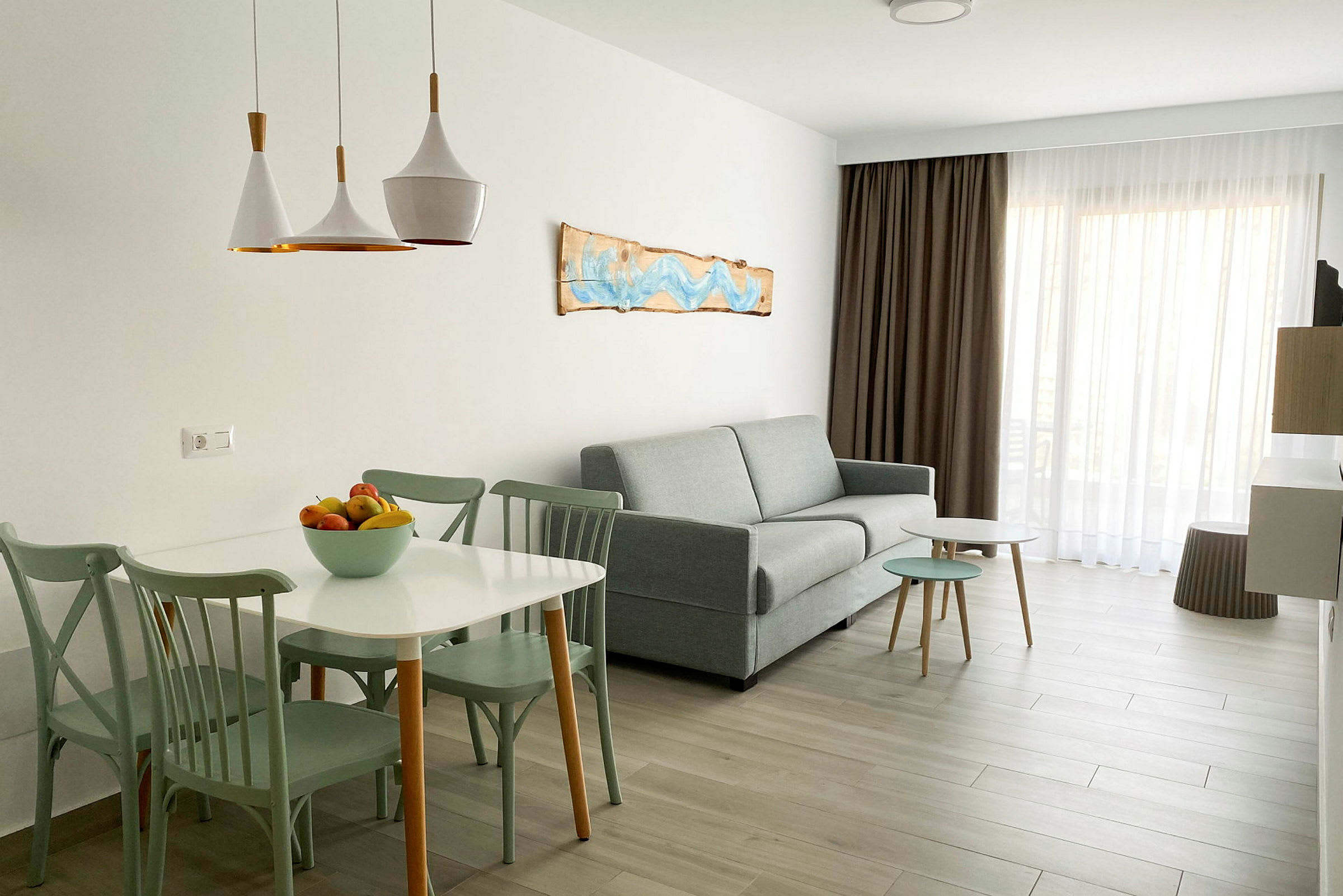En lys og moderne stueinteriør med sofa, bord og stole, samt en skål med frugt på bordet. (AI-genereret tekst)