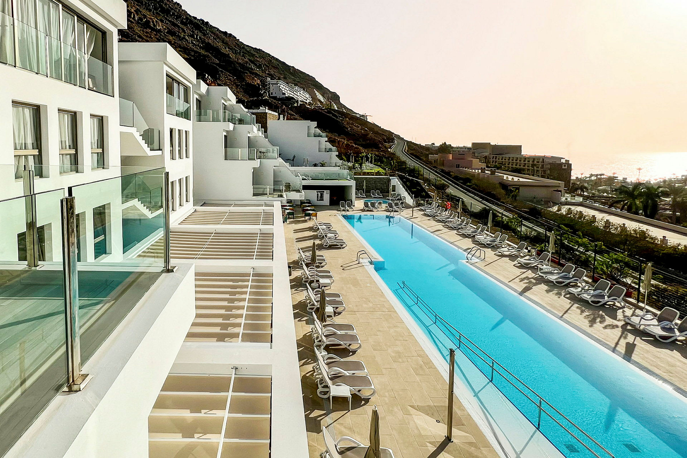 Hotel med hvide bygninger og en lang pool omgivet af liggestole. (AI-genereret tekst)