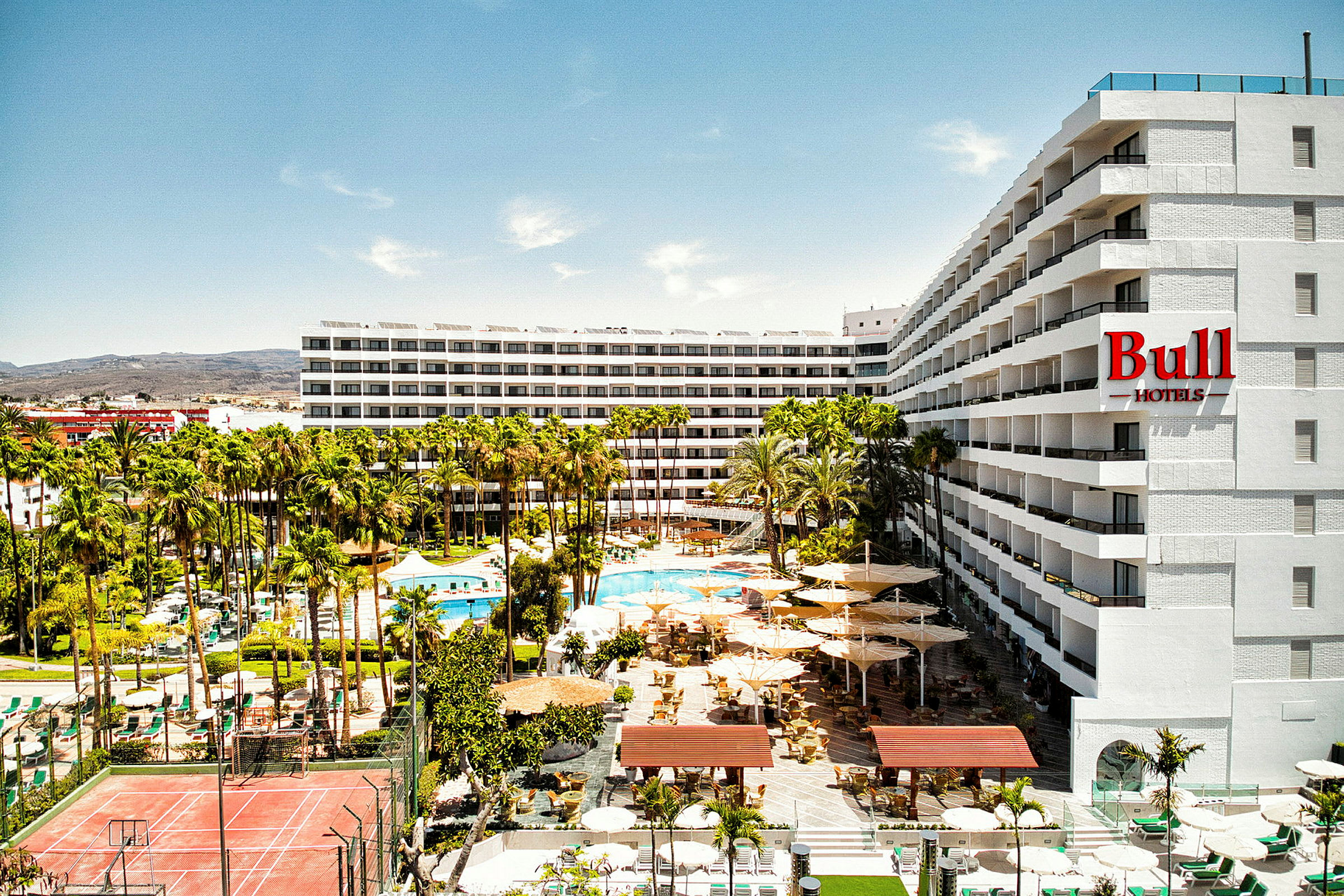 Hotelbygning med en pool og palmetræer i forgrunden. (AI-genereret tekst)