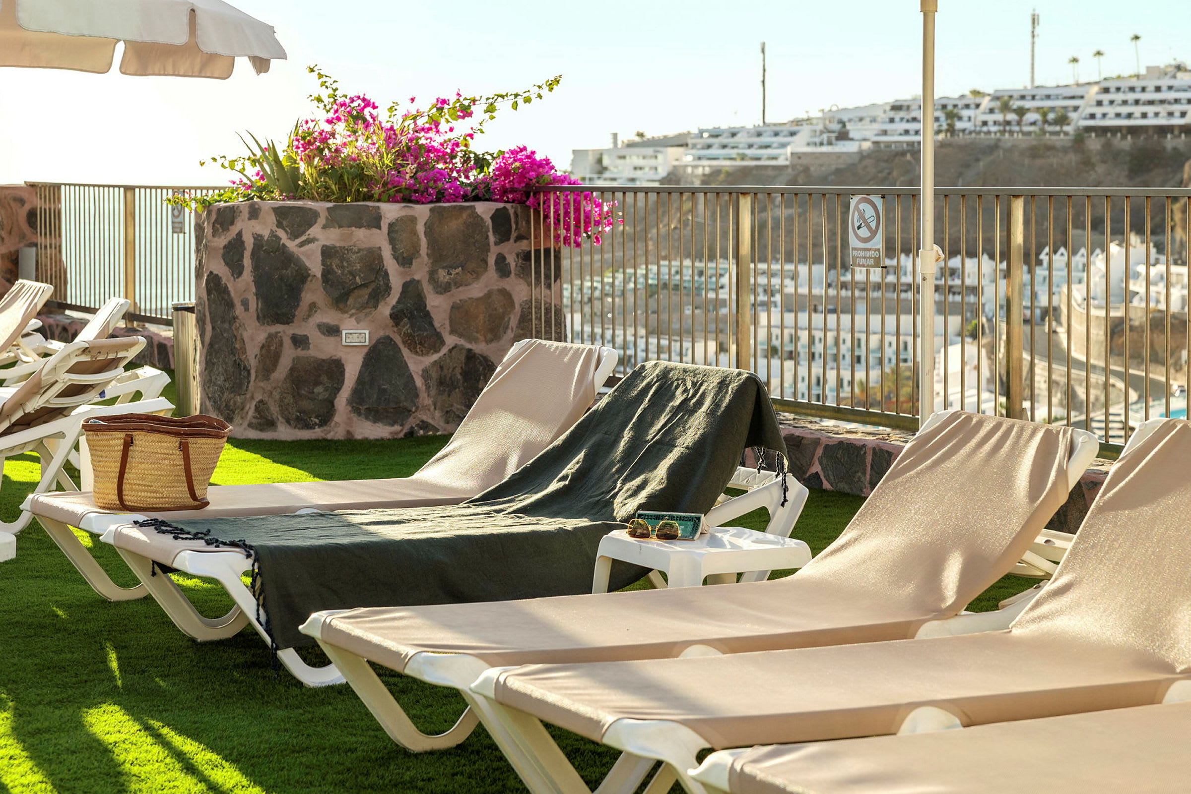 Liggestole på en terrasse med udsigt over en by og blomster i en stenkrukke benyttes. (AI-genereret tekst)