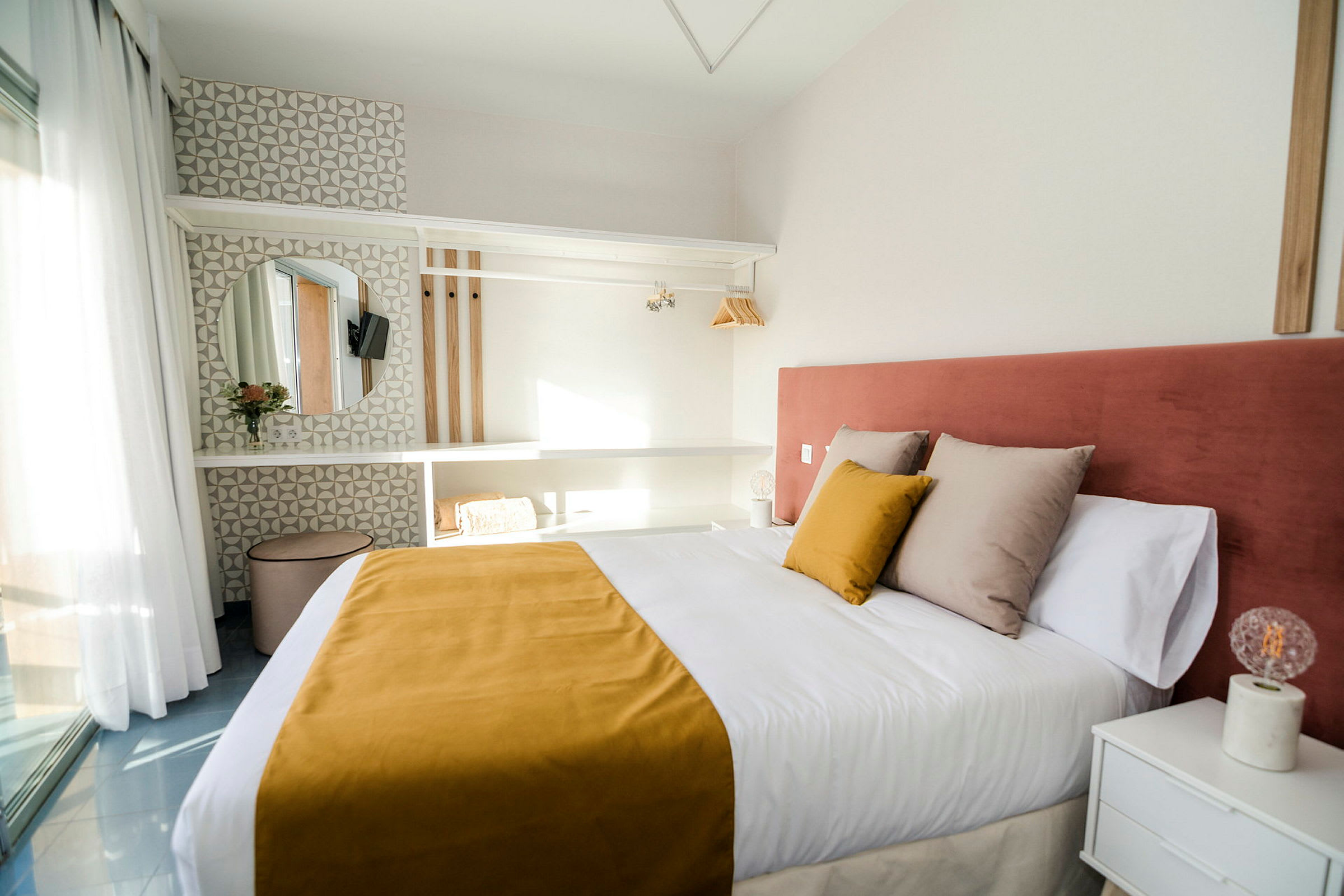 Et hotelværelse med en dobbeltseng, gul sengetæppe og rosa sengegavl samt en moderne indretning med hylder, spejl og lys dekoration. (AI-genereret tekst)