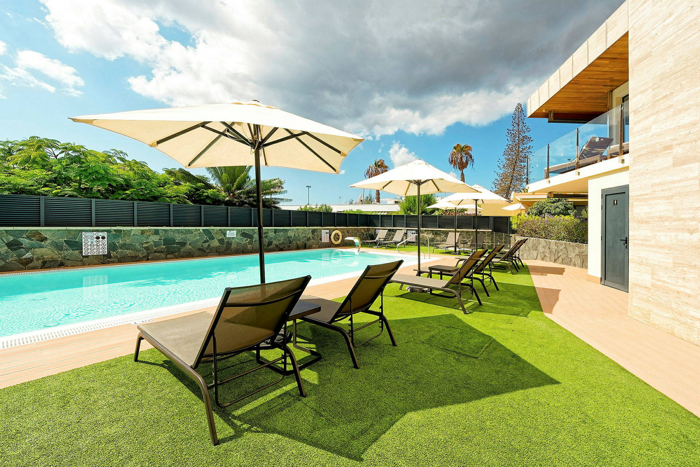 En udendørs pool med liggestole og parasoller på græs og terrasse. (AI-genereret tekst)