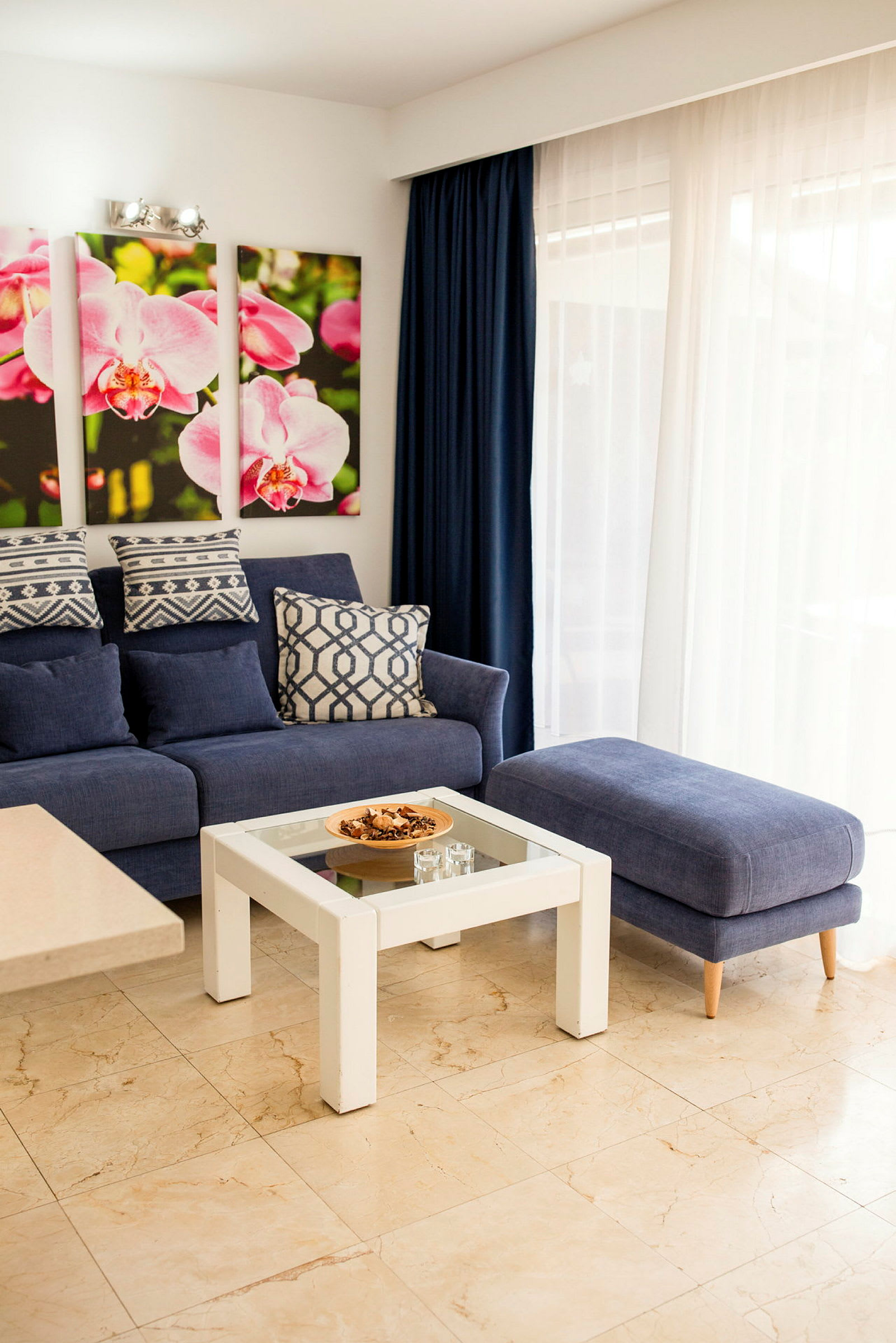 En stue med blå sofa, sofabord og vægdekorationer med lyserøde blomster. (AI-genereret tekst)