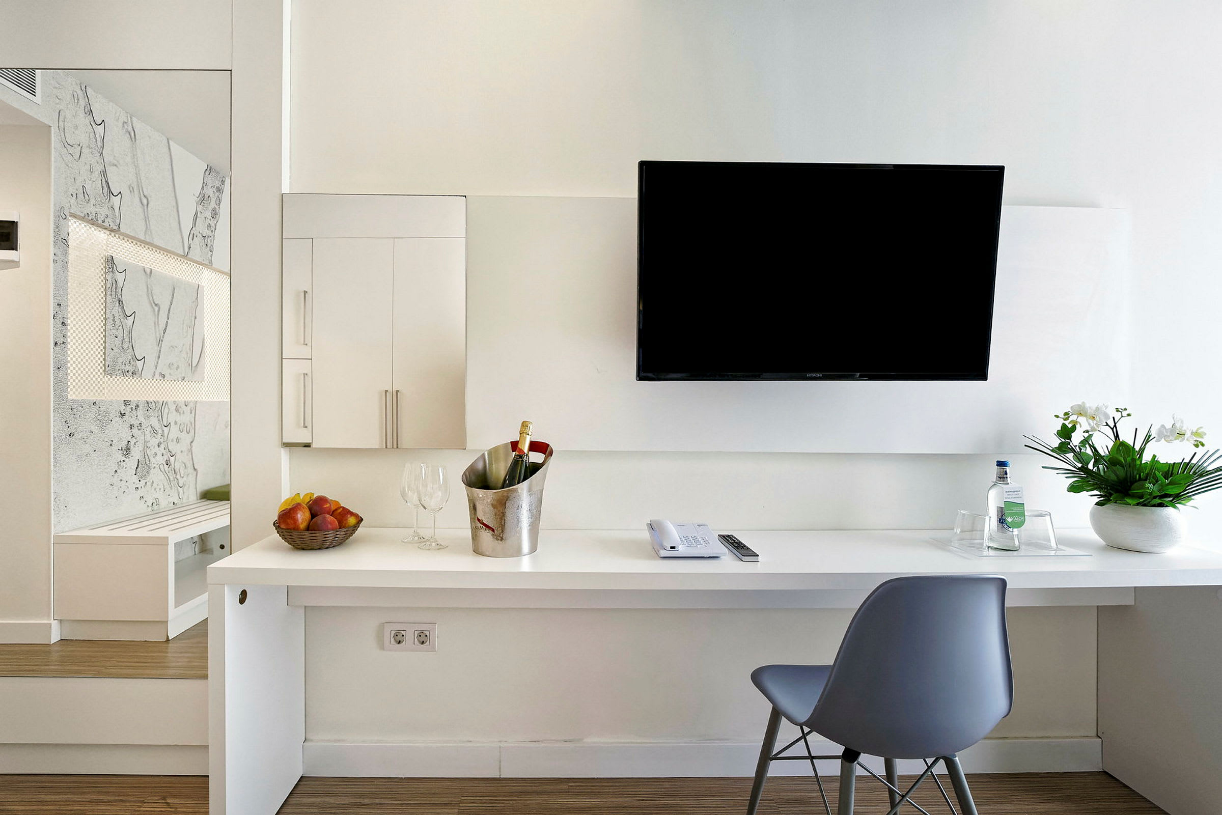 Moderne hotelværelsesindretning med skrivebord, stol, væg-tv, blomsterarrangement og forfriskninger. (AI-genereret tekst)