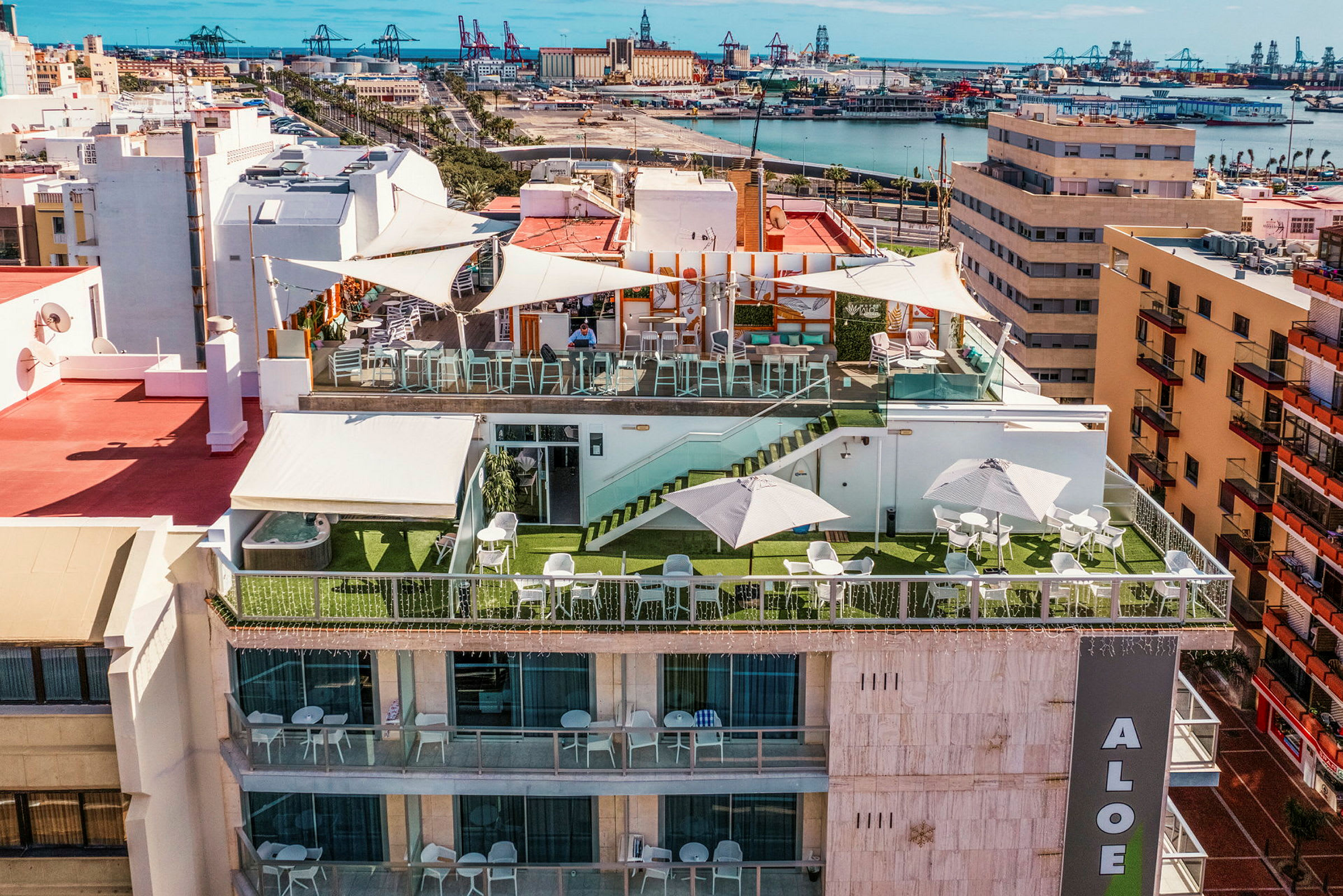 Hotelterrasse med siddeområder, parasoller og udsigt over byen og havnen. (AI-genereret tekst)