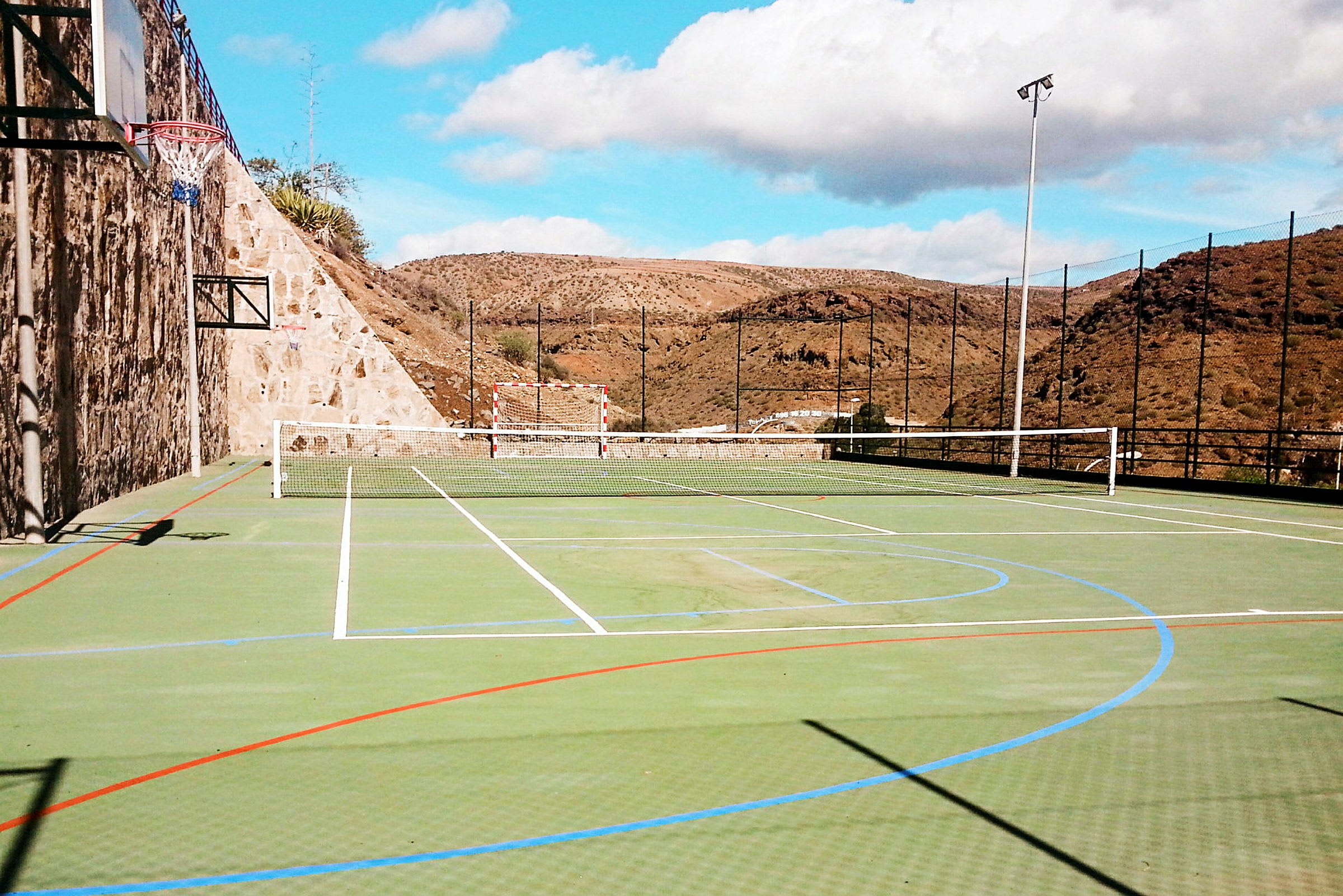 Billede af en udendørs idrætsplads med net til tennis, fodboldmål og basketballkurv. (AI-genereret tekst)