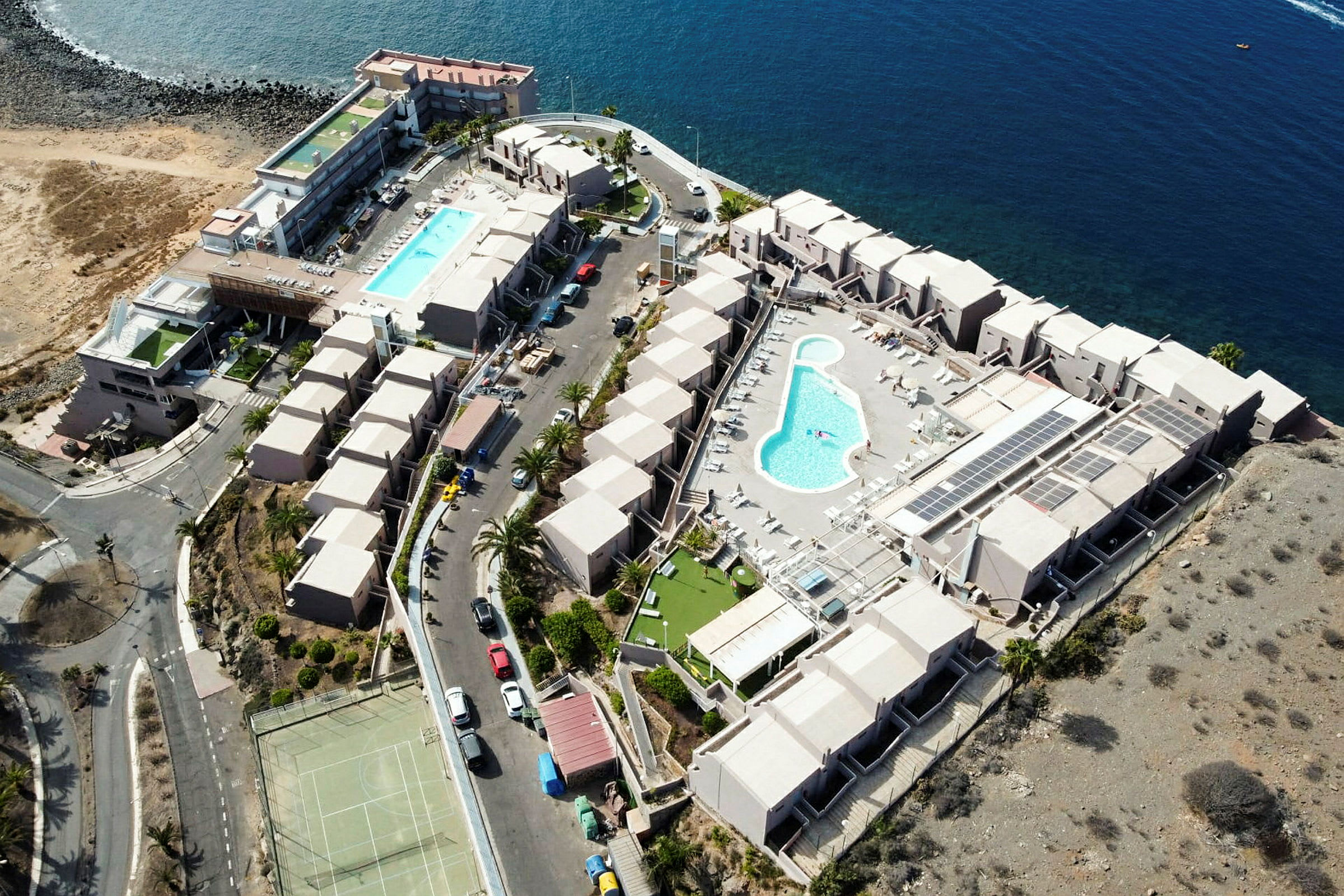 Luftfoto af et stort feriested ved havet med swimmingpools og bygninger. (AI-genereret tekst)