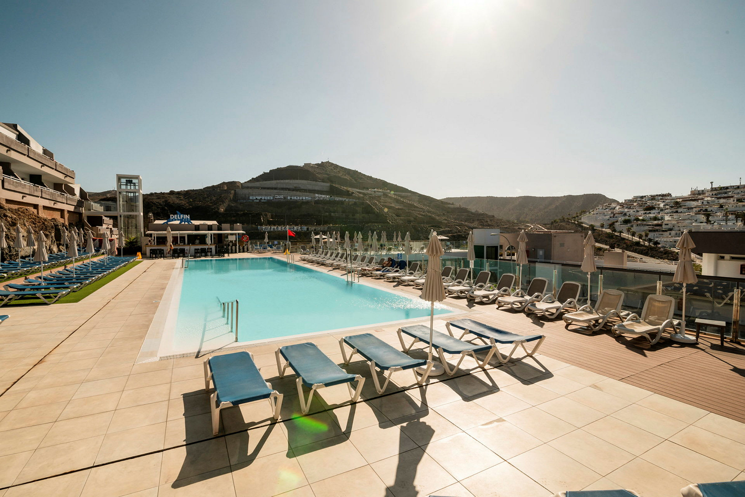 Udendørs udsigt over en hotelpool med liggestole og parasoller på en solrig bjerglokation. (AI-genereret tekst)
