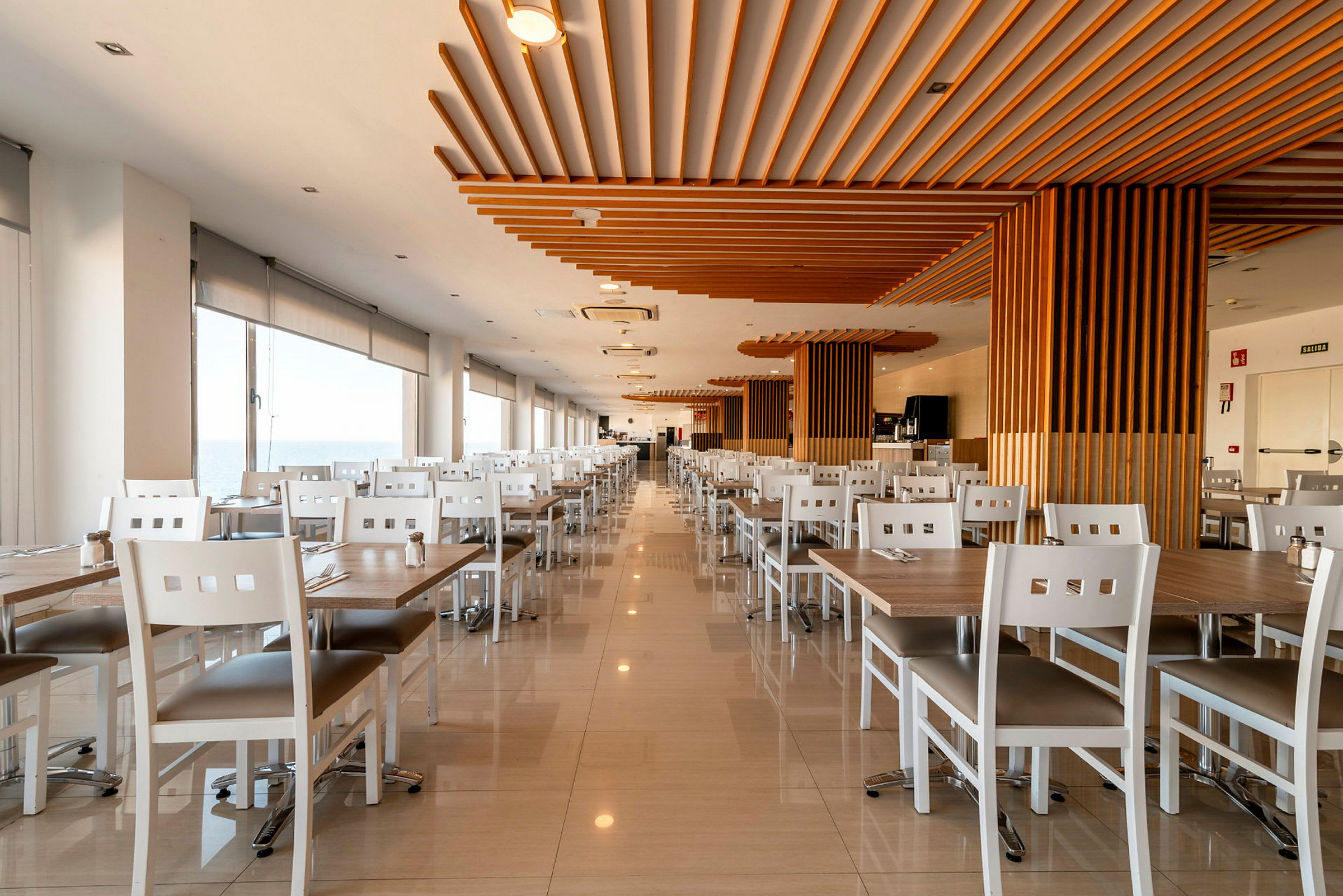 Billede af en rummelig og lys restaurant med hvide borde og stole samt træelementer i loftet. (AI-genereret tekst)