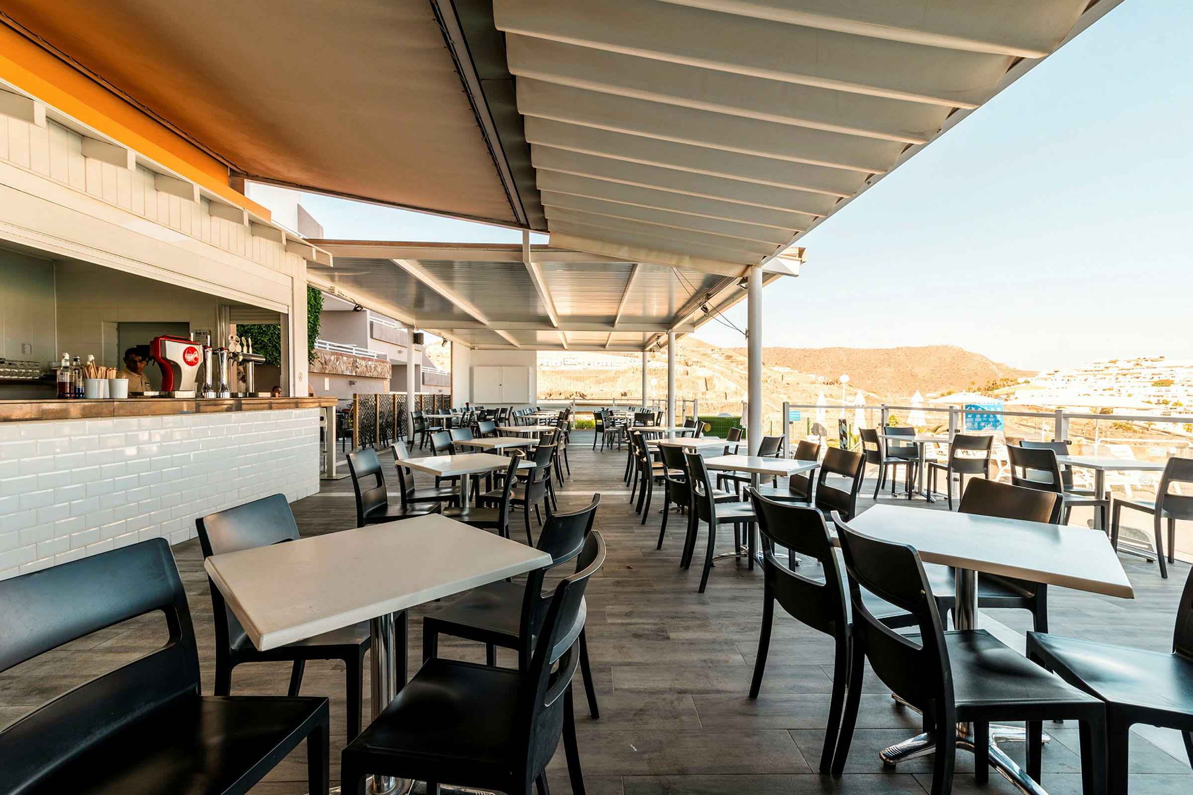 Udendørsrestaurant med moderne borde og stole under en overdækket pergola. (AI-genereret tekst)
