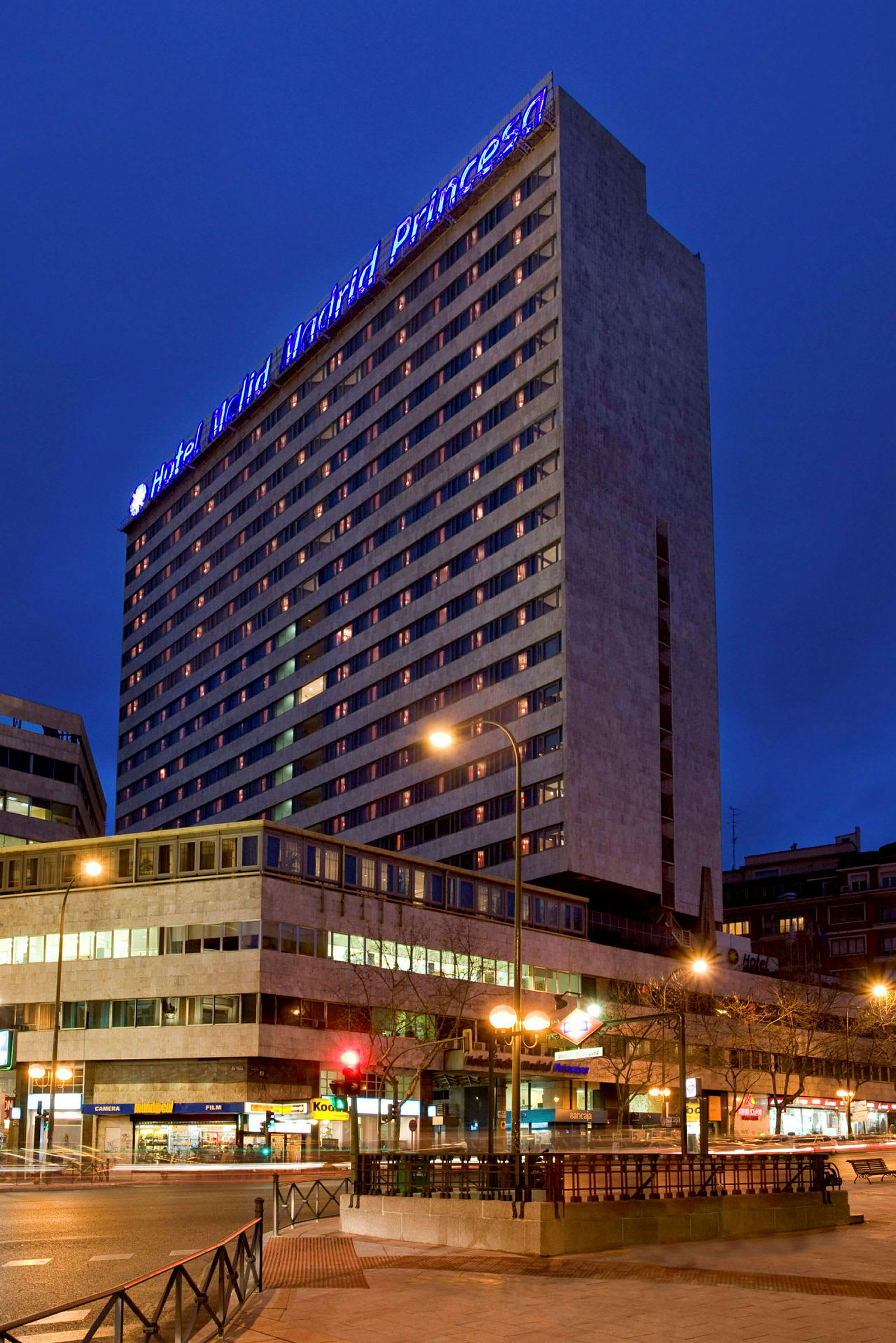 Et hotel om aftenen med oplyste vinduer og et blåt skilt på toppen, der lyser bygningen op. (AI-genereret tekst)