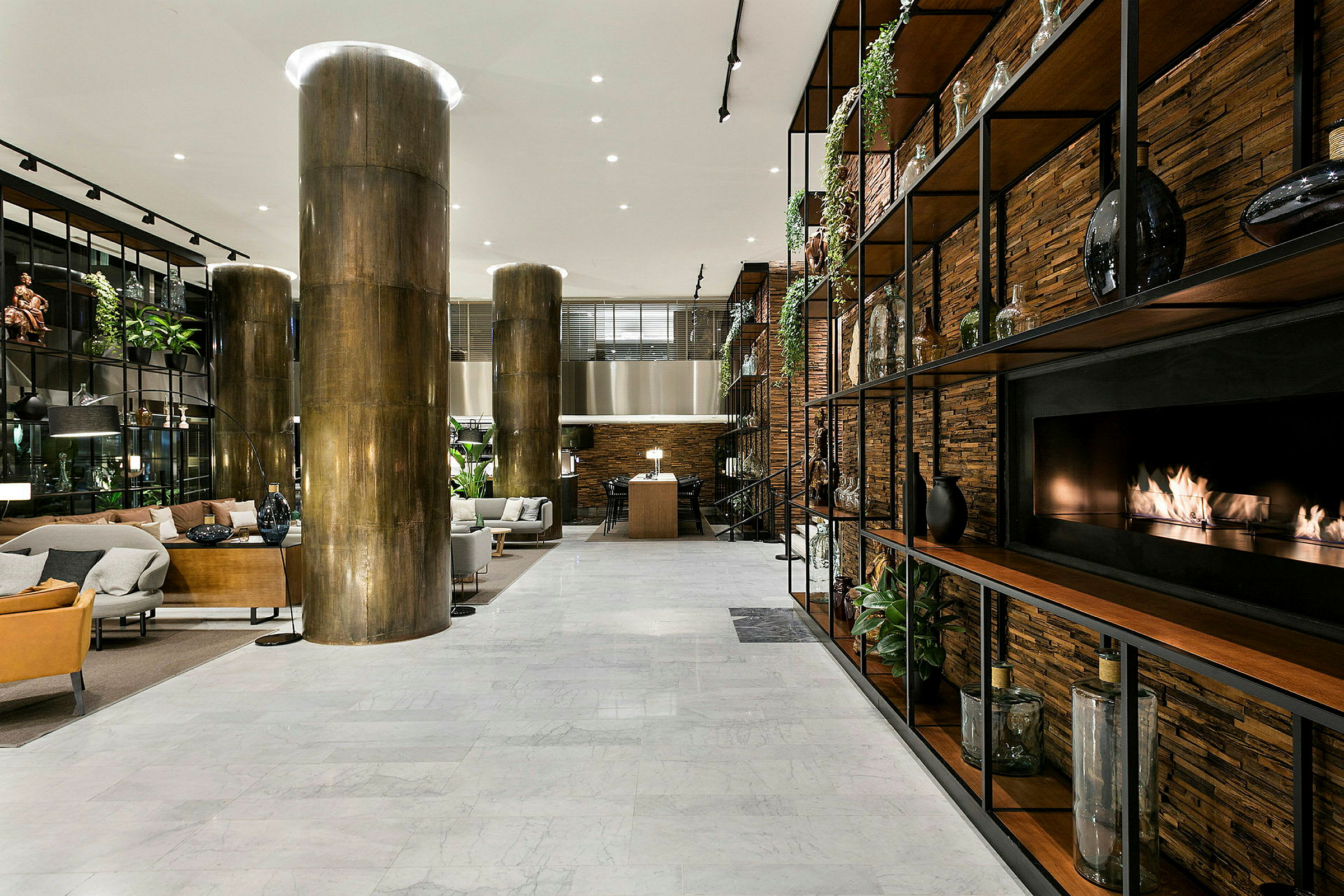 Et moderne hotellobbyområde med siddeområder, marmorgulv, store søjler og en pejs integreret i en hyldevæg. (AI-genereret tekst)