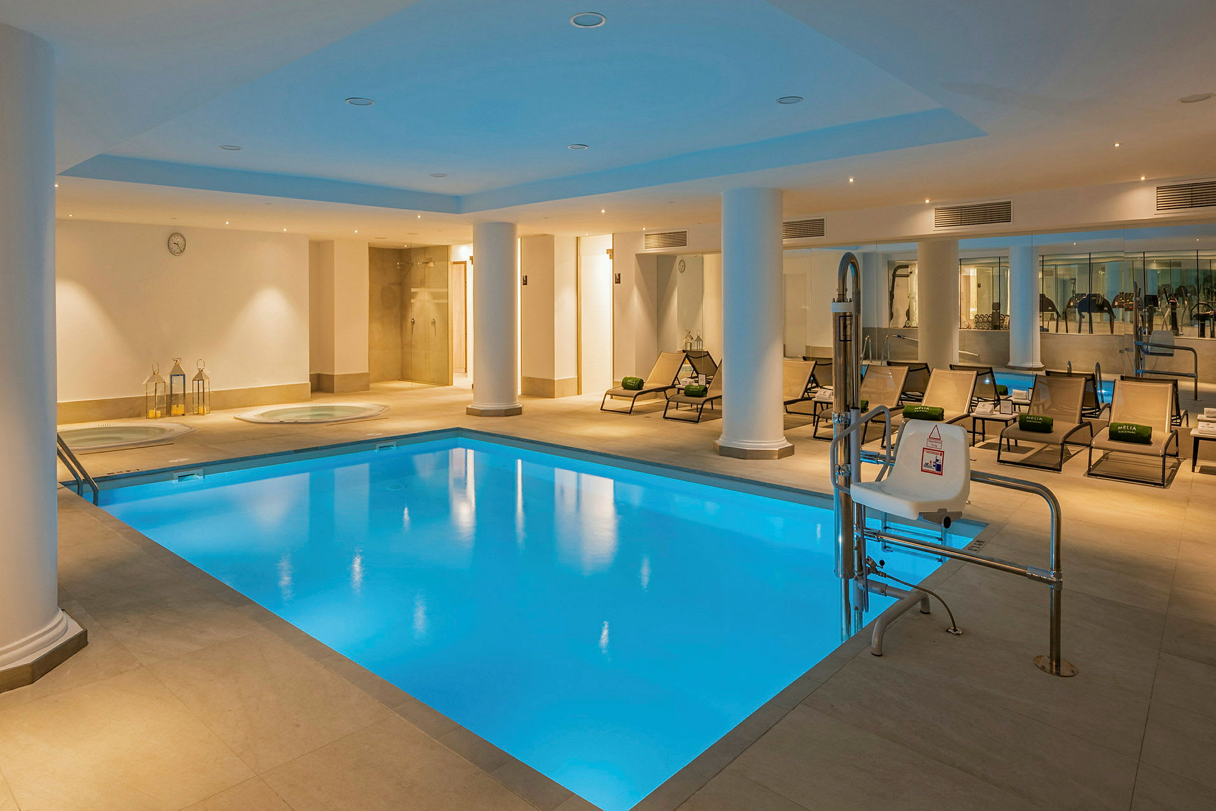 En indendørs pool med liggestole og søjler omkring. I baggrunden ses et wellness-område. (AI-genereret tekst)