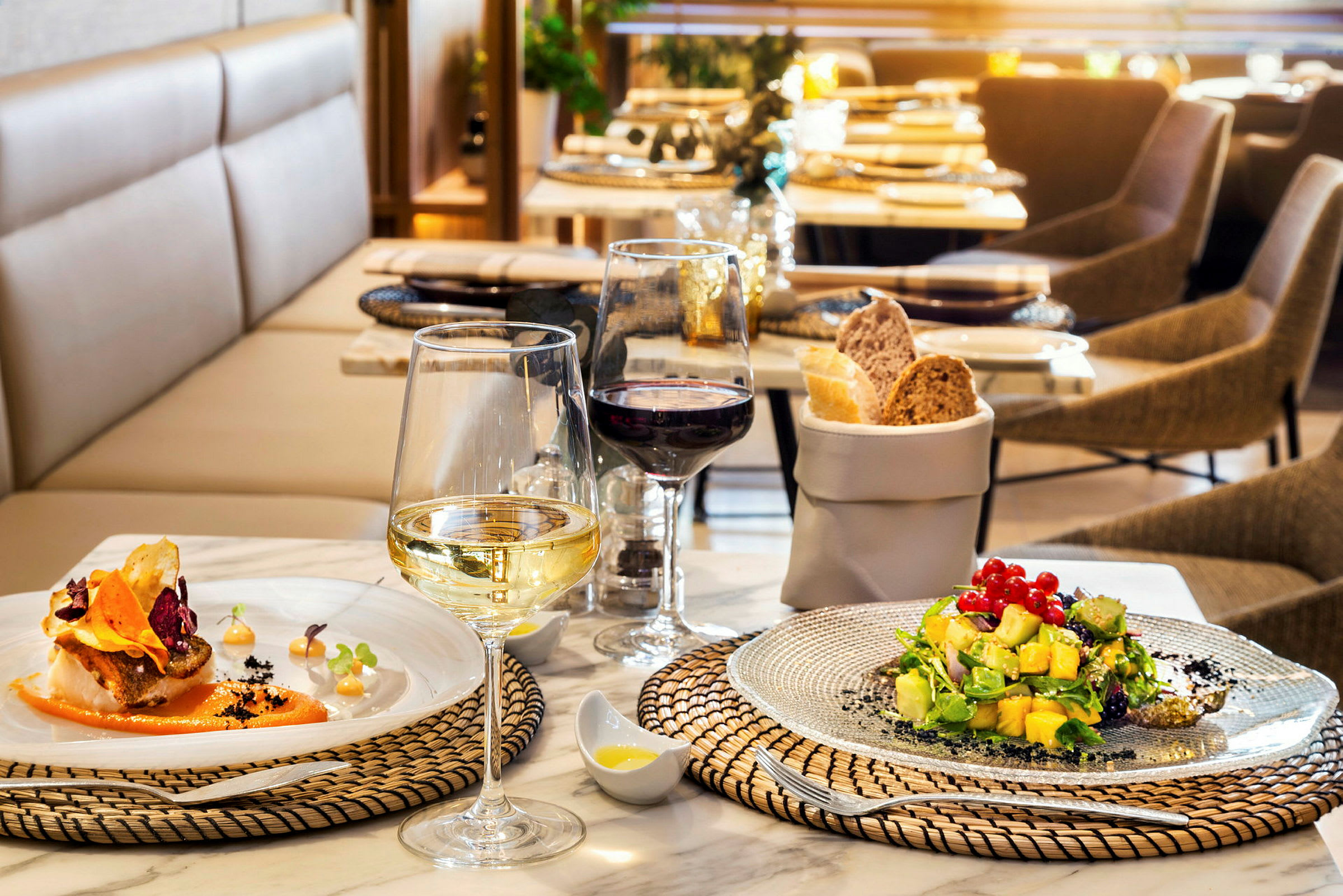 Et dækket bord på en restaurant med to tallerkener med mad, vinglas og en brødkurv. (AI-genereret tekst)
